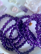 Overhead view of deep purple amethyst crystal bead bracelets on a white plate with mini crystals in the background