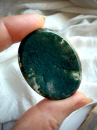 Moss Agate oval worry stone held in hand with dense forest green dendritic inclusions