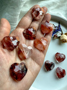Array of faceted Fire Quartz mini crystal hearts displayed on hand – natural healing stones for grounding, balance, and spiritual support