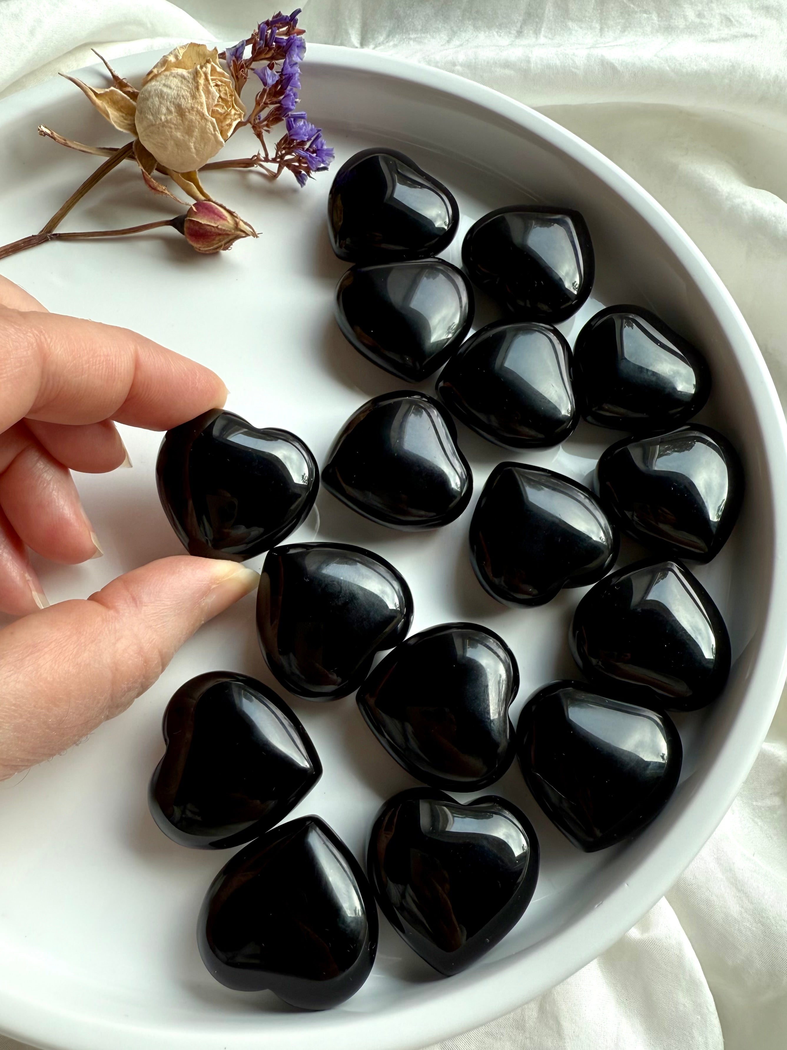 Close-up of multiple Black Obsidian hearts on a plate, hand selecting one of the crystals.