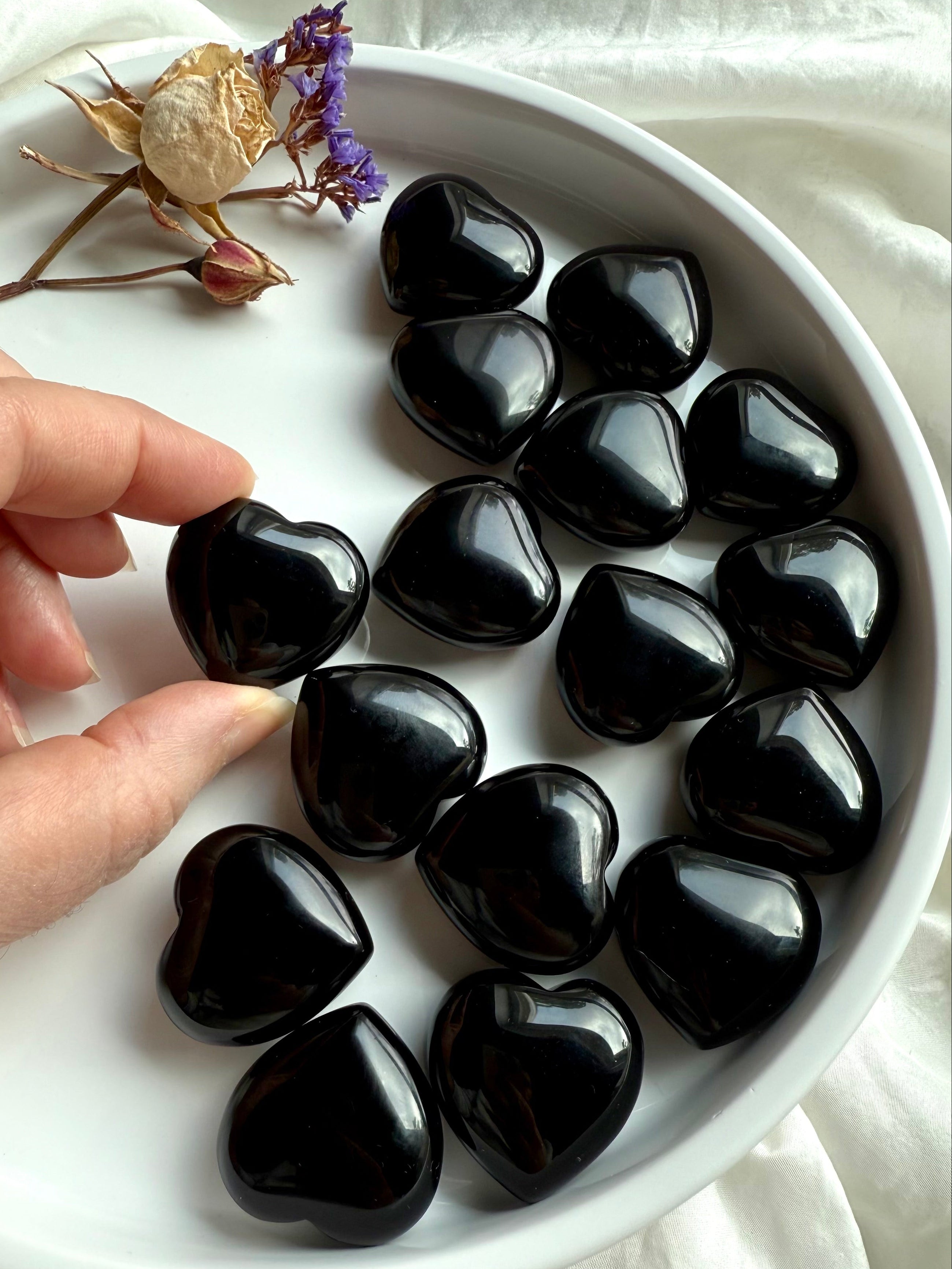 Close-up of multiple Black Obsidian hearts on a plate, hand selecting one of the crystals.