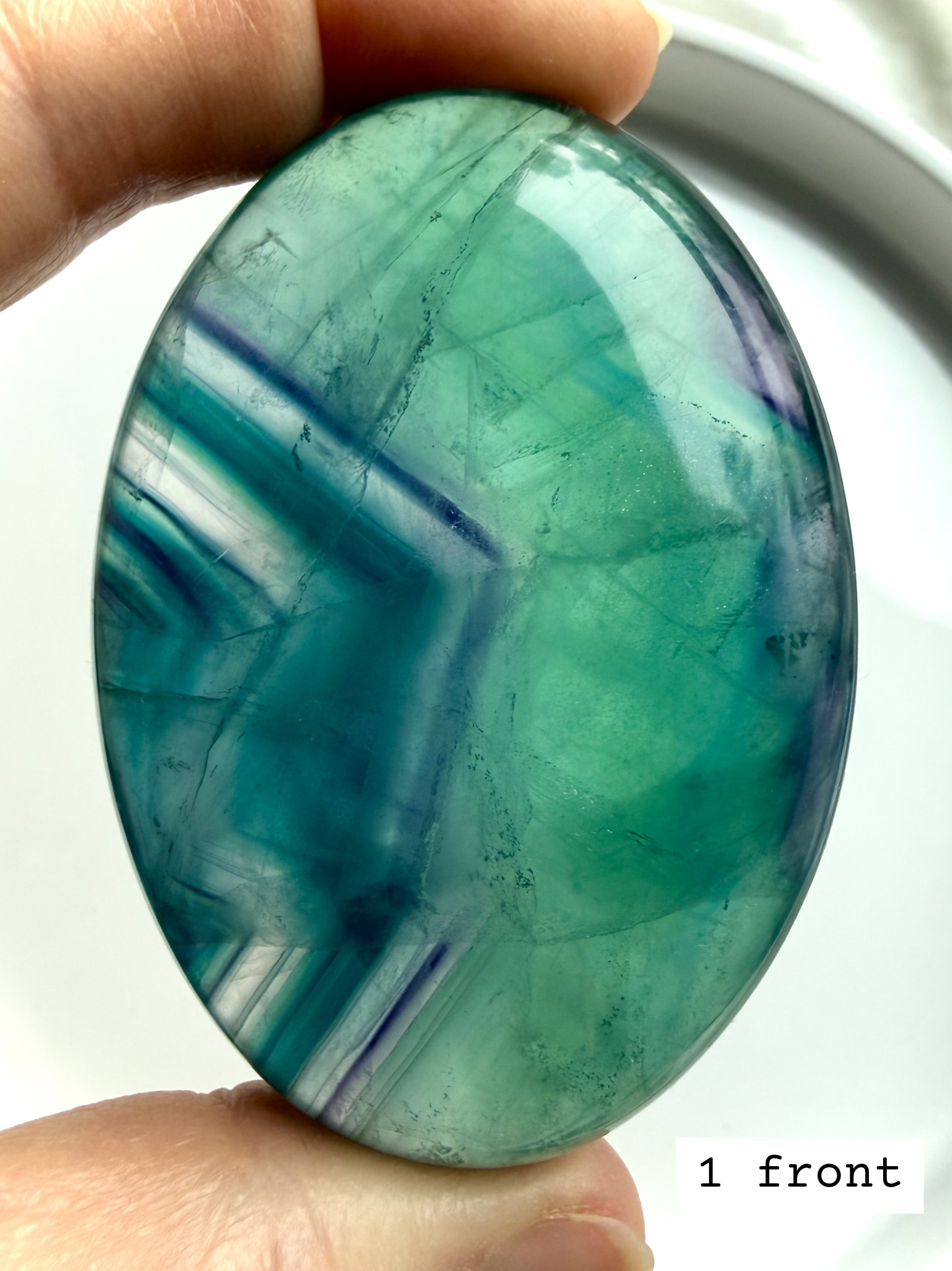 Teal fluorite palm stone #1 front view held to the light, showing vibrant blue green banding and luminous translucency