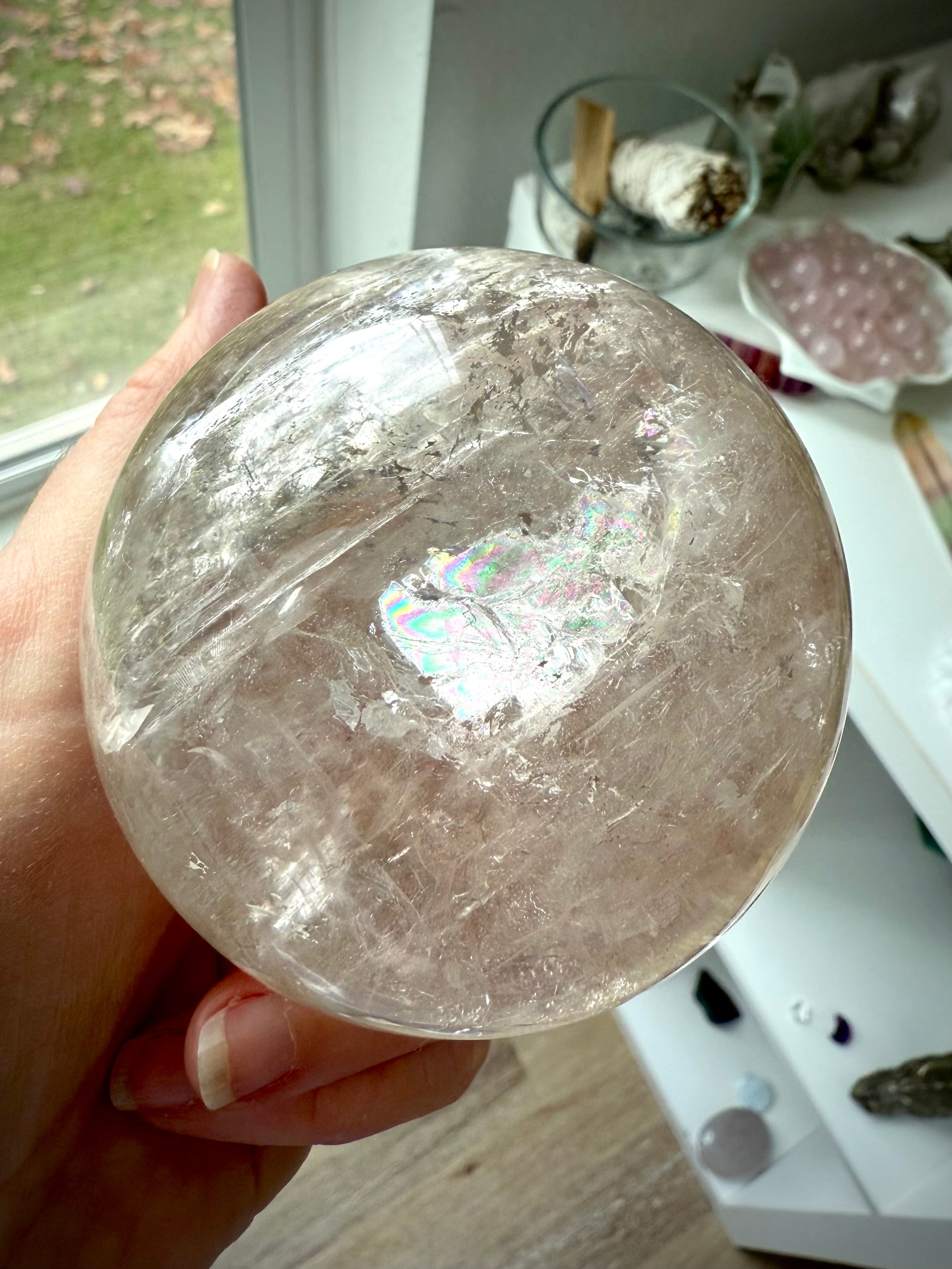 A hand holding a Champagne Smokey Quartz Sphere with visible silver flash and rainbow inclusions.