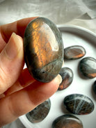 Peach Sunset Labradorite palm stone held in hand with vibrant orange, peach, and golden flash