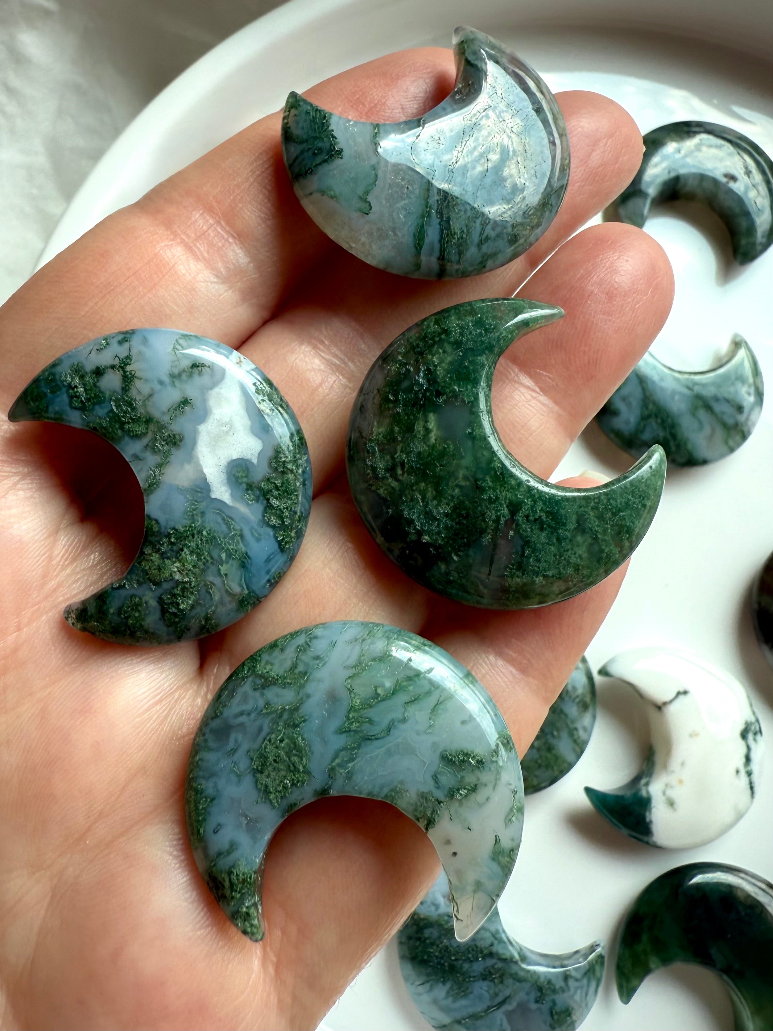Close-up of four Moss Agate crescent moon crystals in hand showing variation in color, pattern, and translucence.