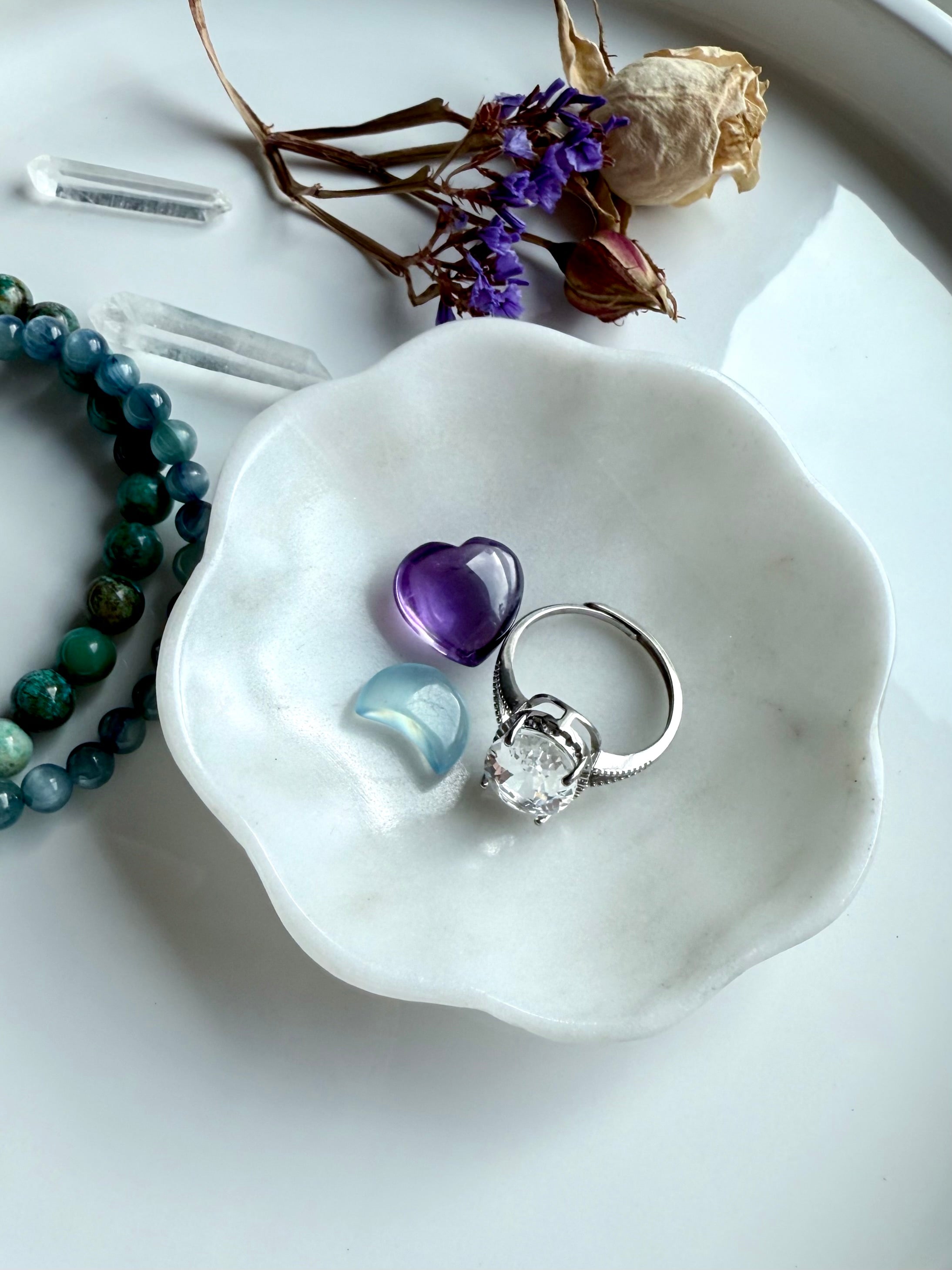 White marble daisy bowl with scalloped flower edges holding an amethyst heart carving, aquamarine moon carving, and silver ring