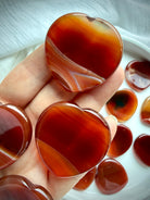 Carnelian heart worry stones held in hand with rich red-orange tones, natural banding and smooth thumb indentations