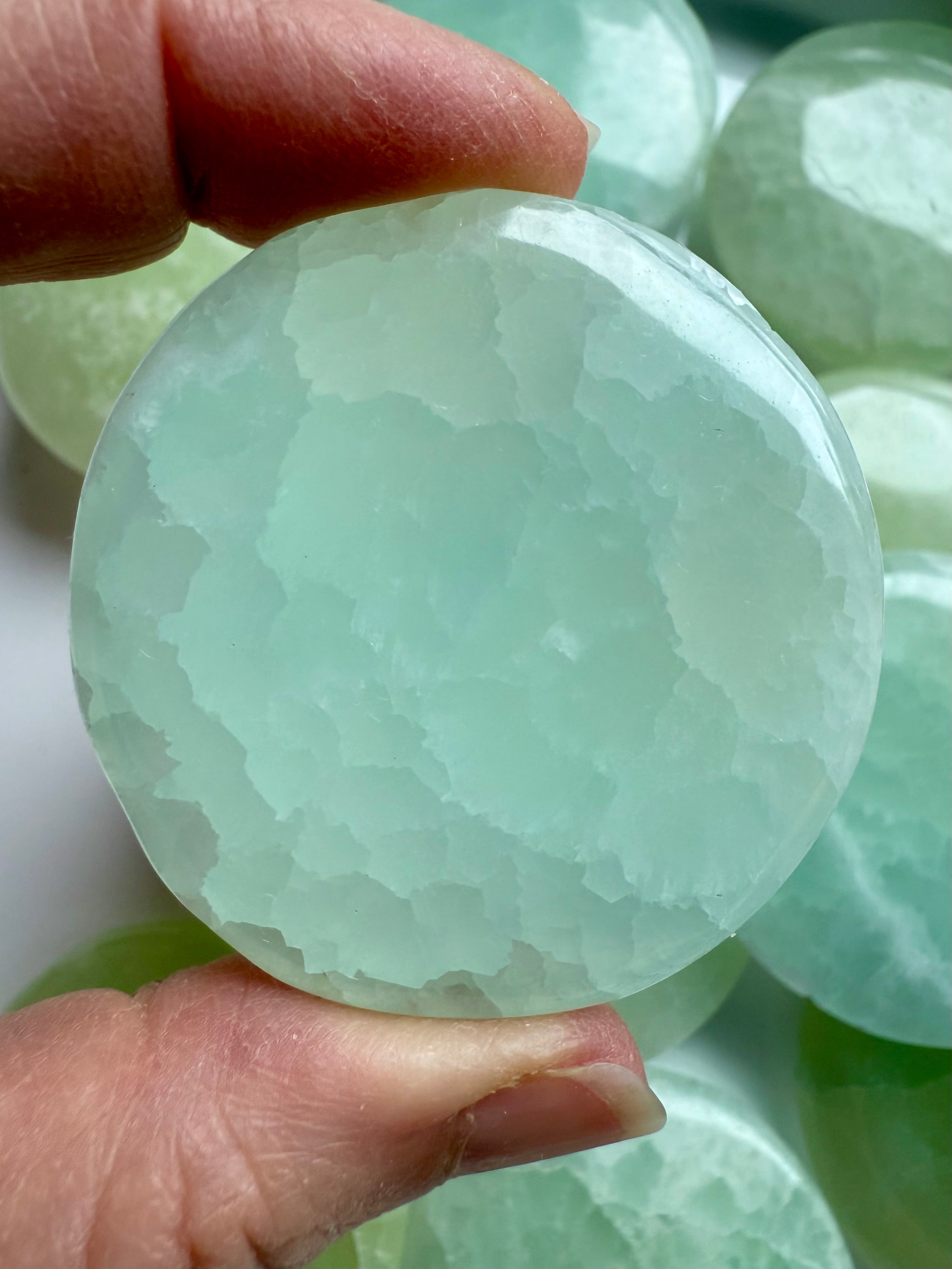 Hand holding a polished Pistachio Calcite disc with soft green and aqua blue tones, glowing with peaceful energy