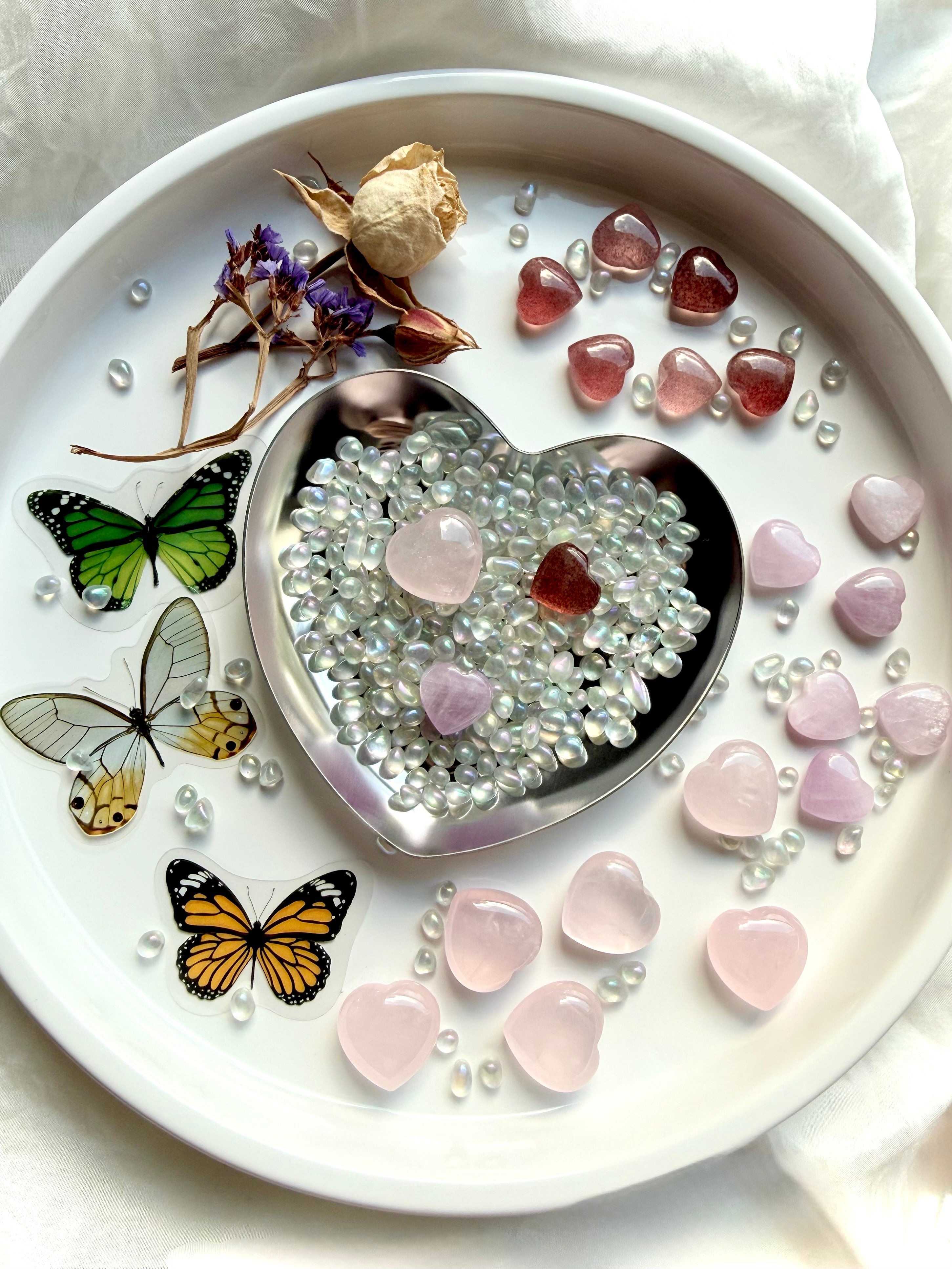 Array of crystal heart sets styled with rose quartz, strawberry quartz, and kunzite mini heart carvings surrounded by aura crystal confetti and butterfly accents