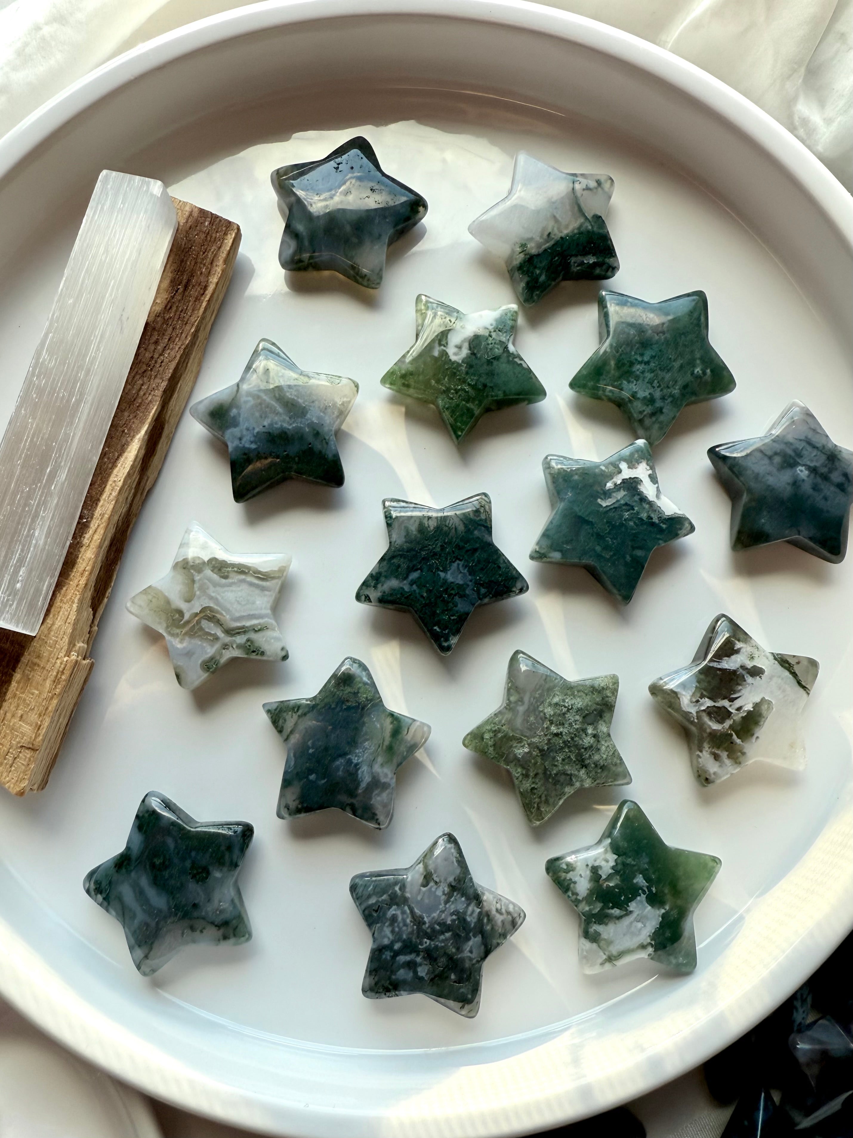 moss agate star crystal carvings displayed in a white dish with selenite and palo santo, showing green dendritic patterns and heart chakra healing energy