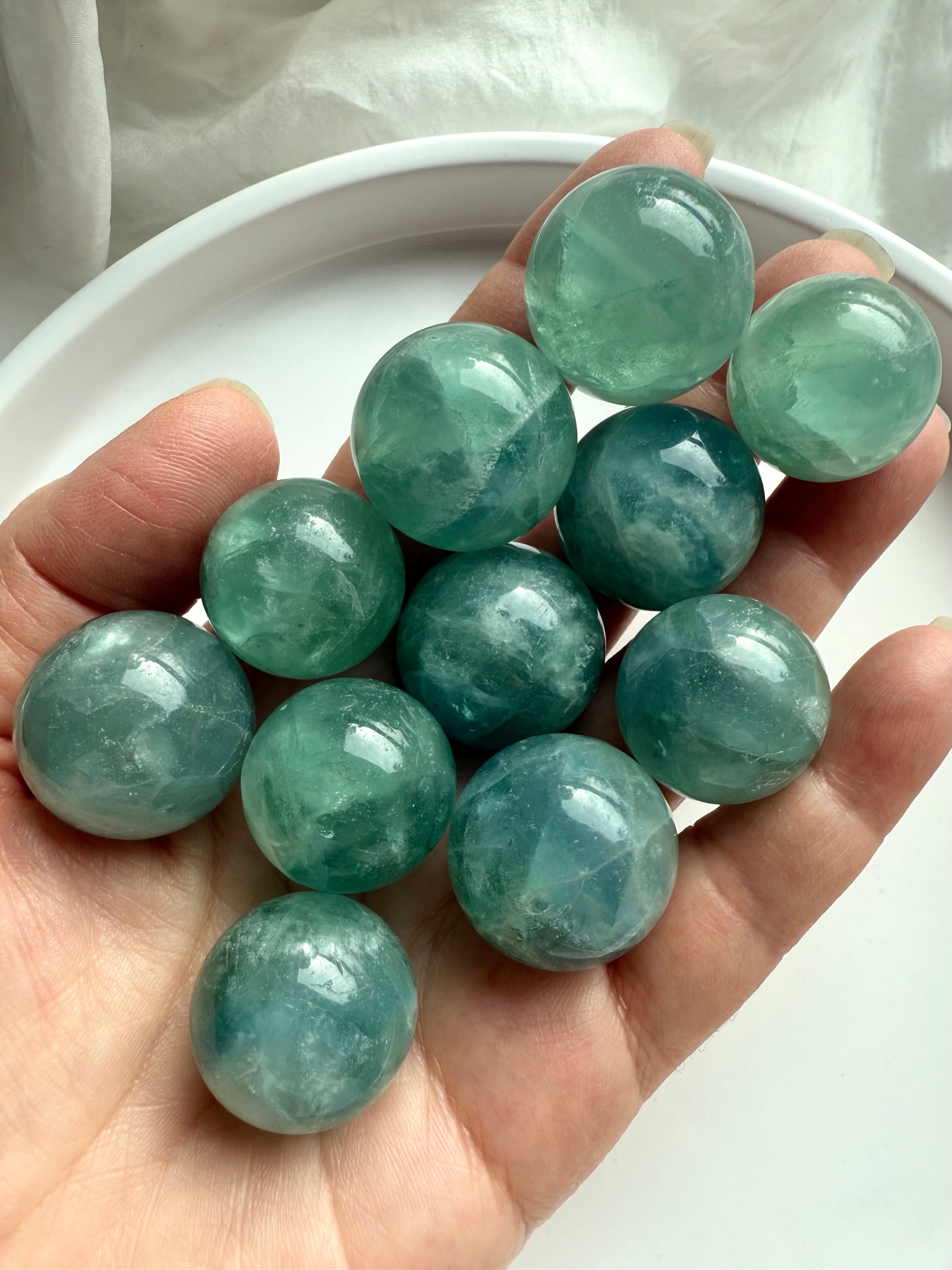 Hand holding several teal Fluorite mini spheres, soothing aqua green crystal balls for focus and balance.
