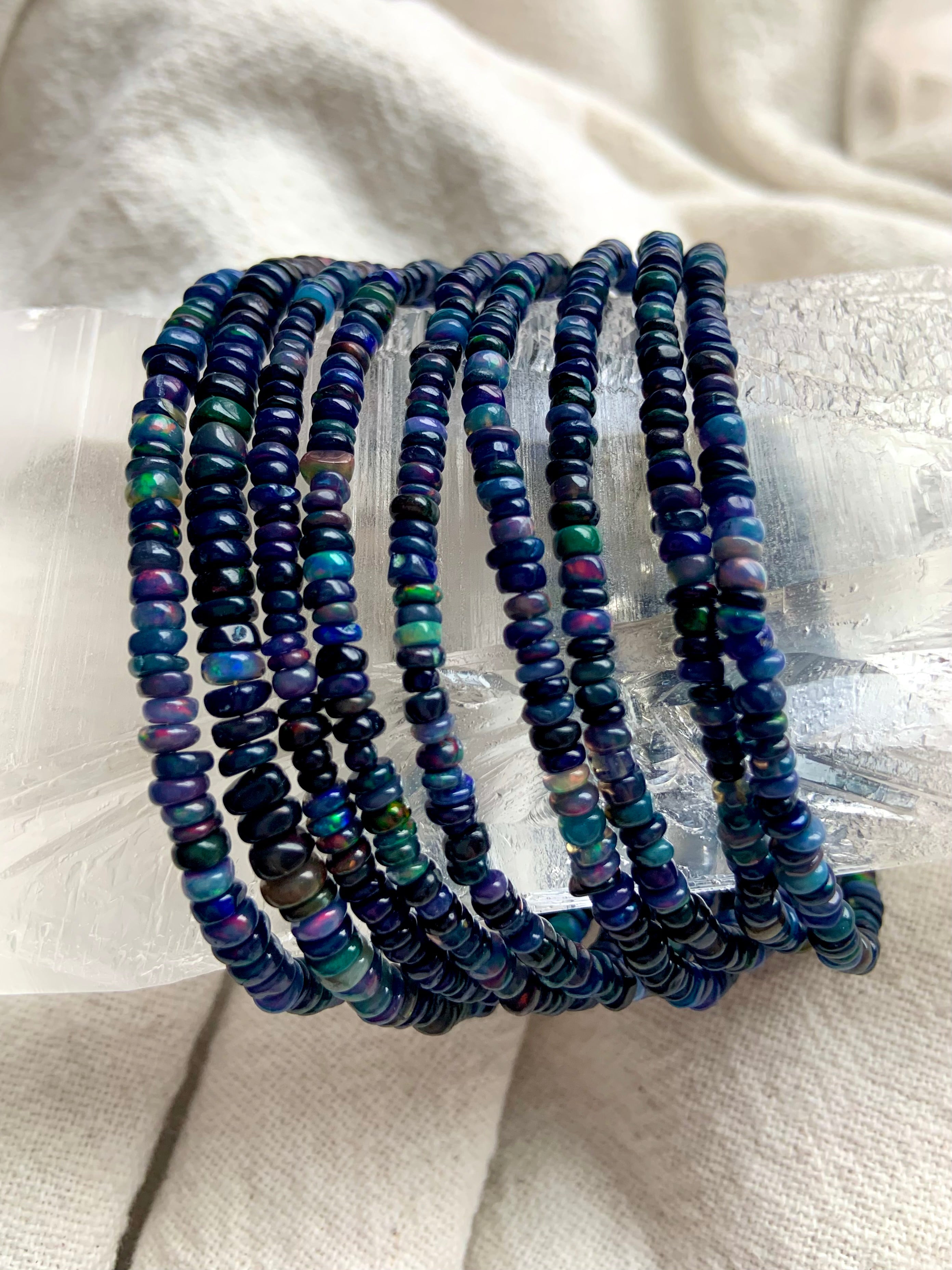 Black Fire Opal bracelets draped over a large clear quartz point — shimmering Ethiopian opal jewelry for October birthdays.