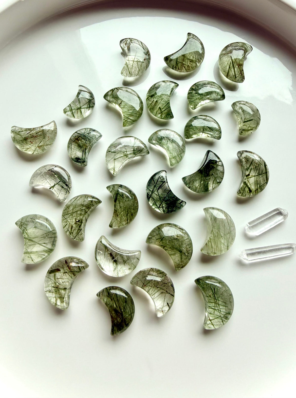 Green Tourmaline in Quartz moons on a white plate, green crystal carvings for Heart Chakra energy and abundance