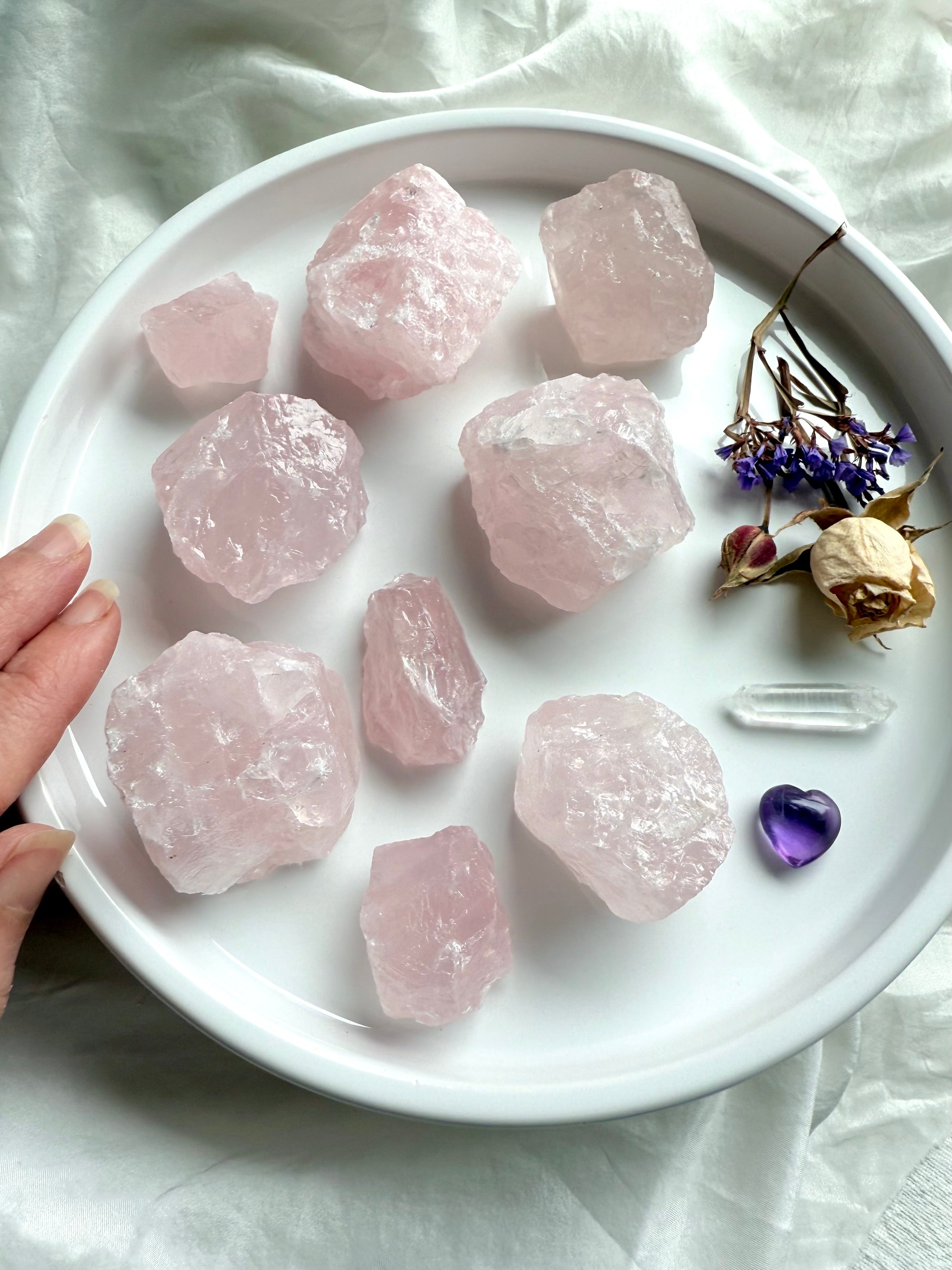 Raw Rose Quartz chunks from Madagascar in mixed sizes on white plate with roses, quartz point, and amethyst heart — Heart Chakra crystals for love and healing