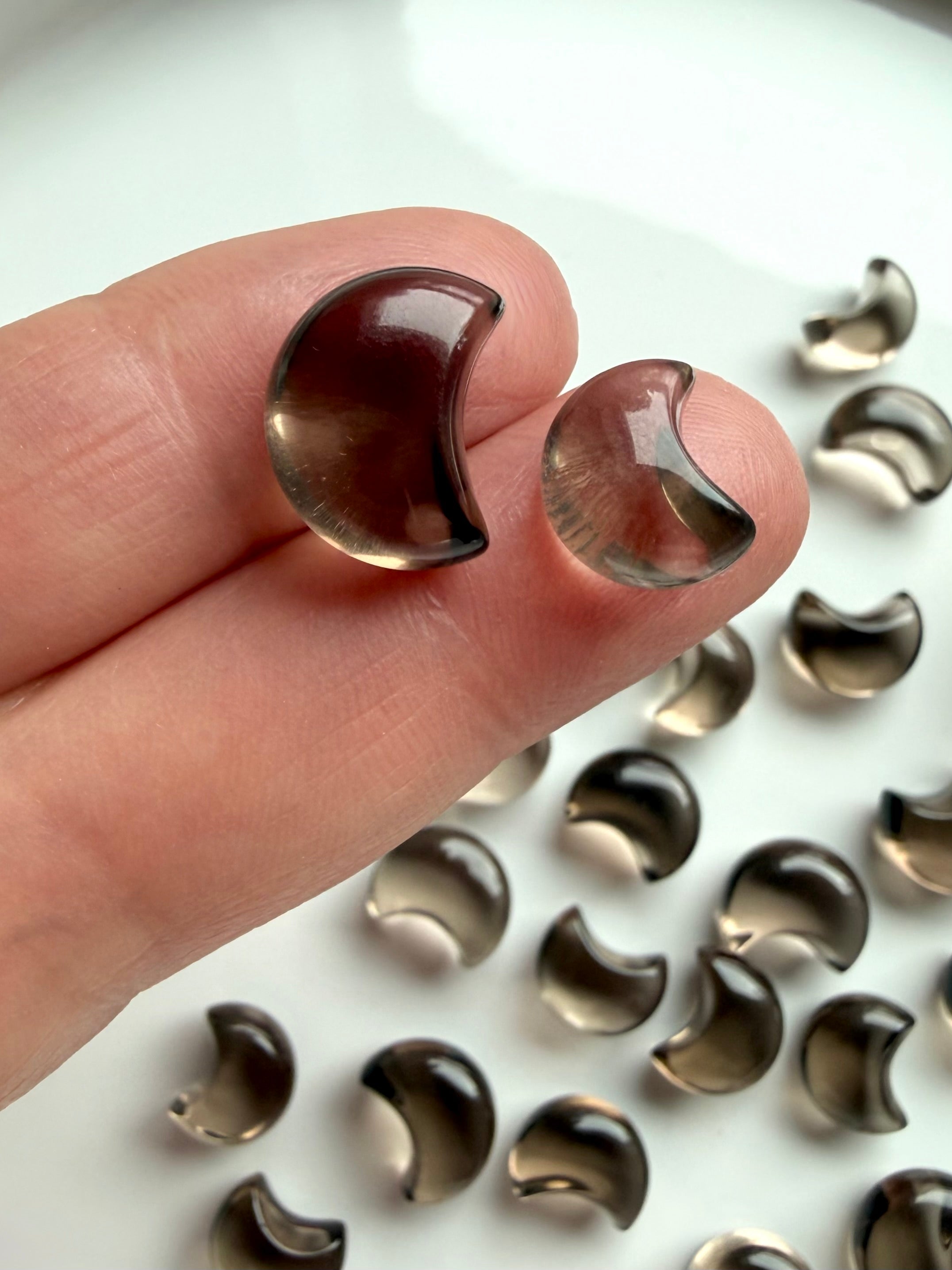 Mini Smoky Quartz moons held between fingers showing tiny crescent crystal size, glossy polish and natural smoky translucence