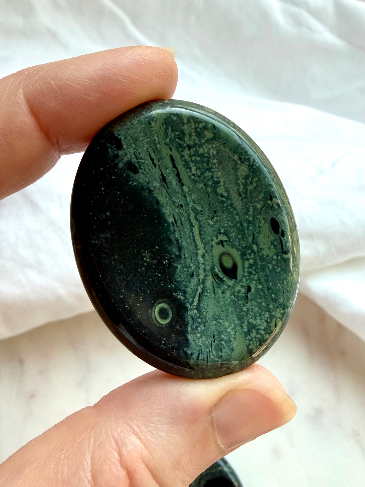 Kambaba Jasper worry stone held in hand showing size, glossy polish, and distinctive green and black natural patterns 
