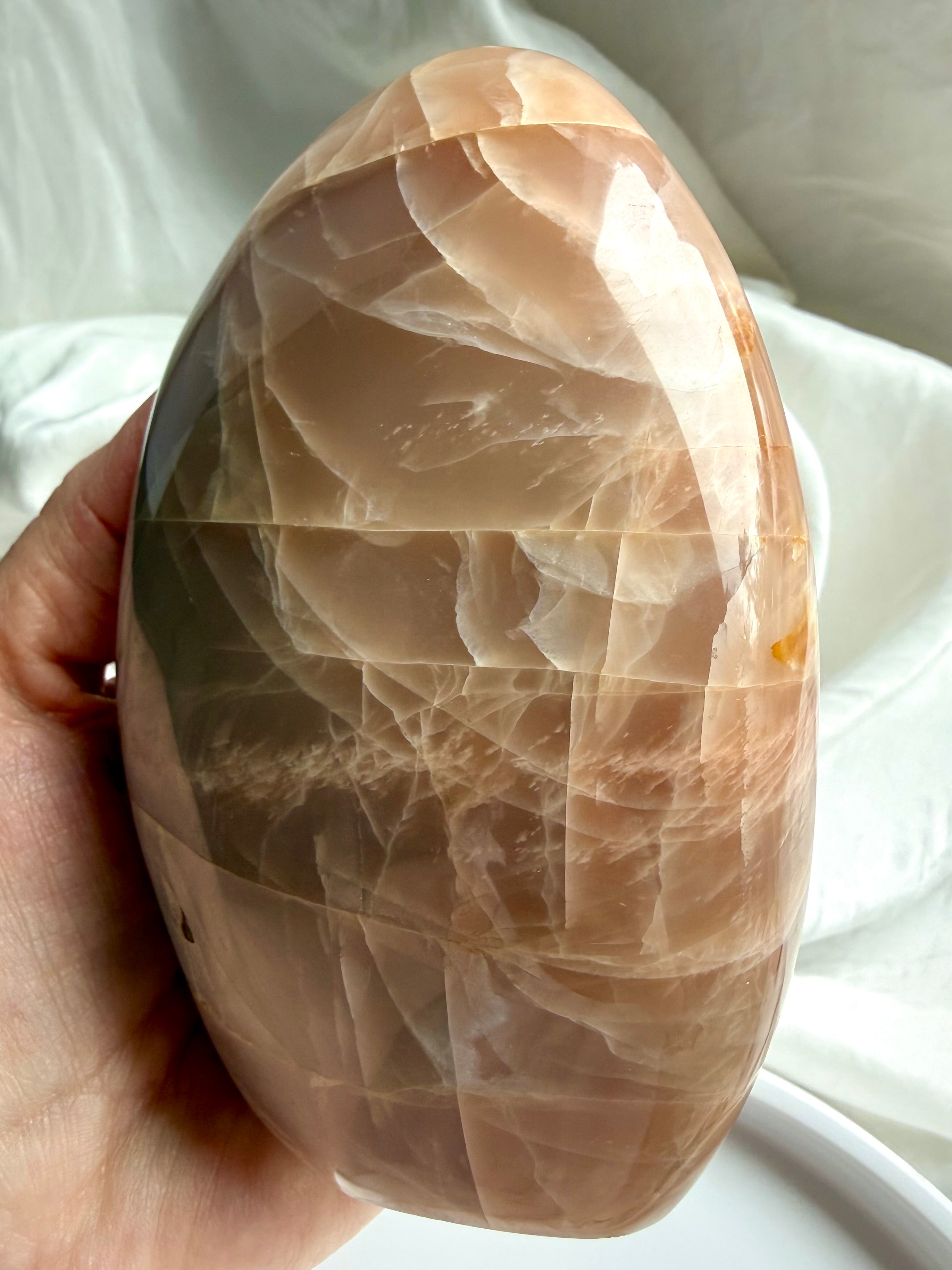 Peach Moonstone freeform crystal with luminous flash and polished surface shown in natural sunlight