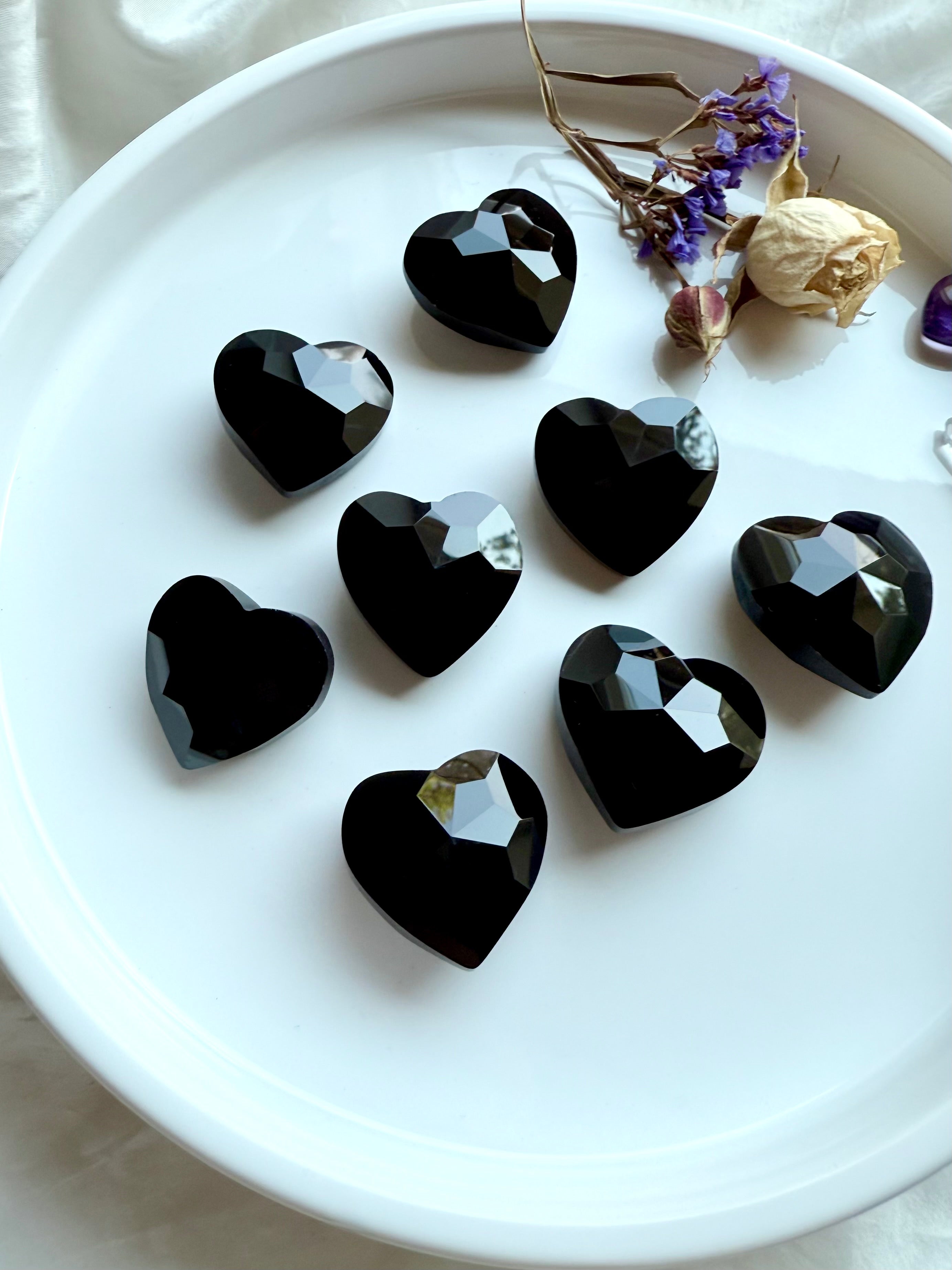 Gem cut crystal hearts in Black Obsidian on a white plate with dried flowers.