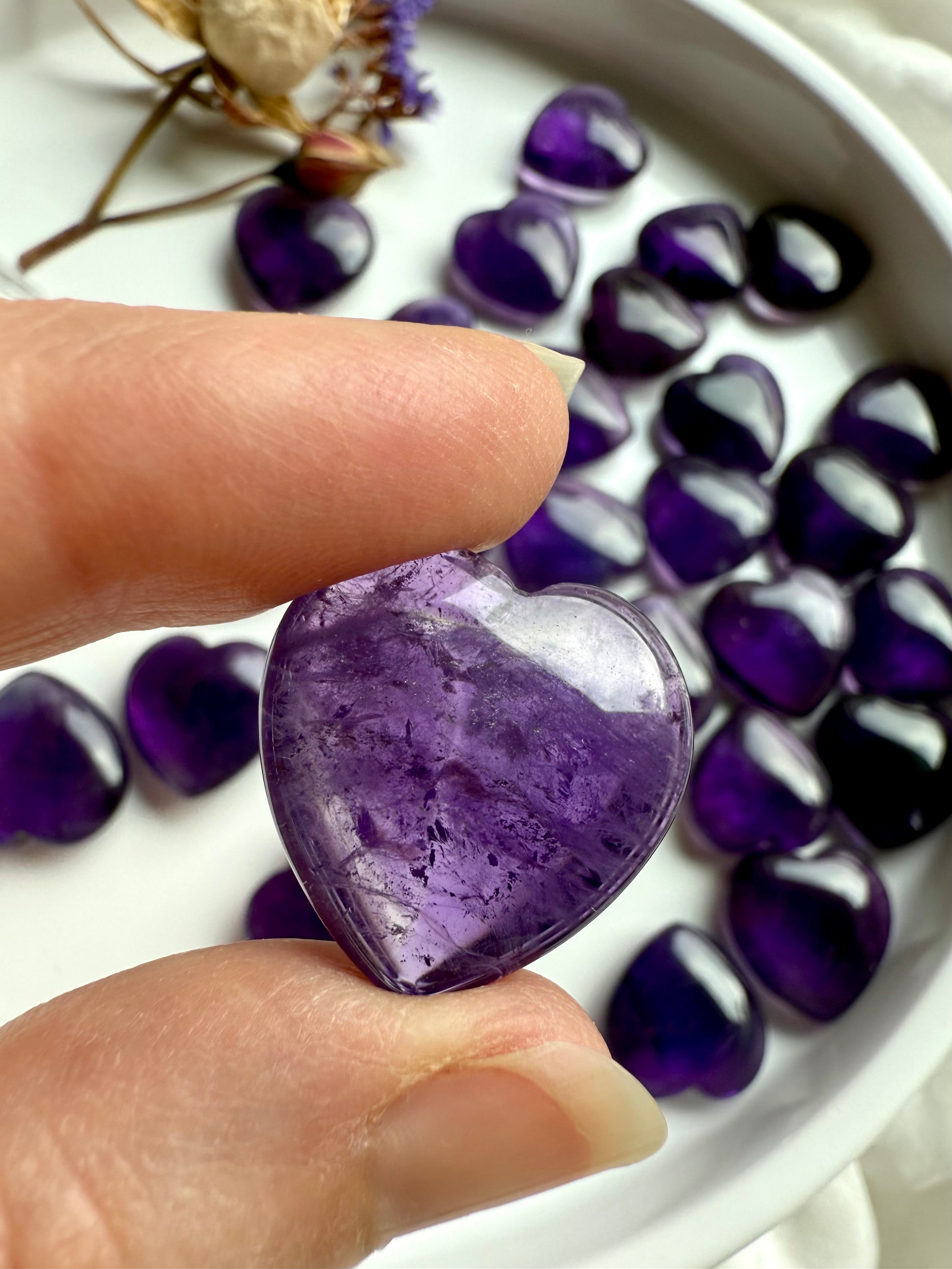 Amethyst heart held between fingertips showing its luminous purple hue — a crown chakra healing stone for intuition, clarity, and spiritual protection.