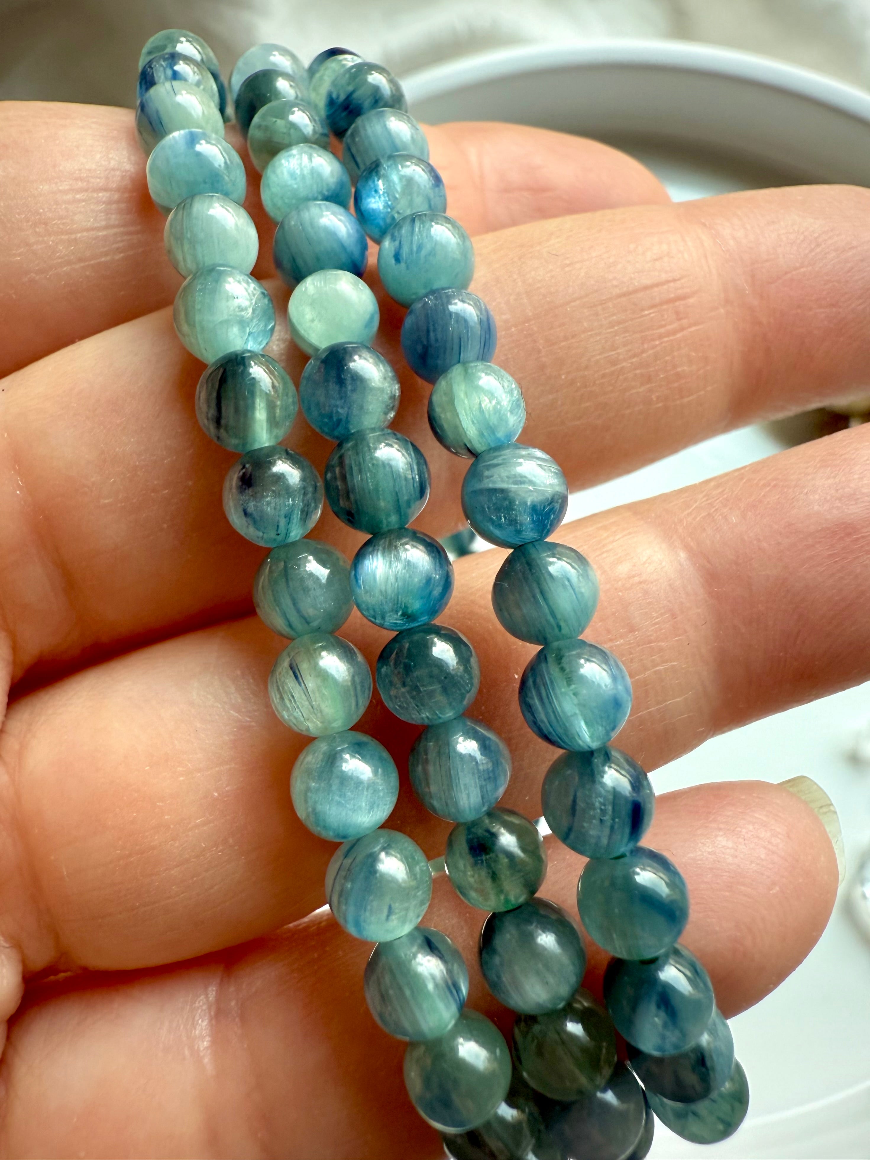 three polished kyanite bracelets in hand revealing fibrous gemstone texture and color variation in calming blue-green tones