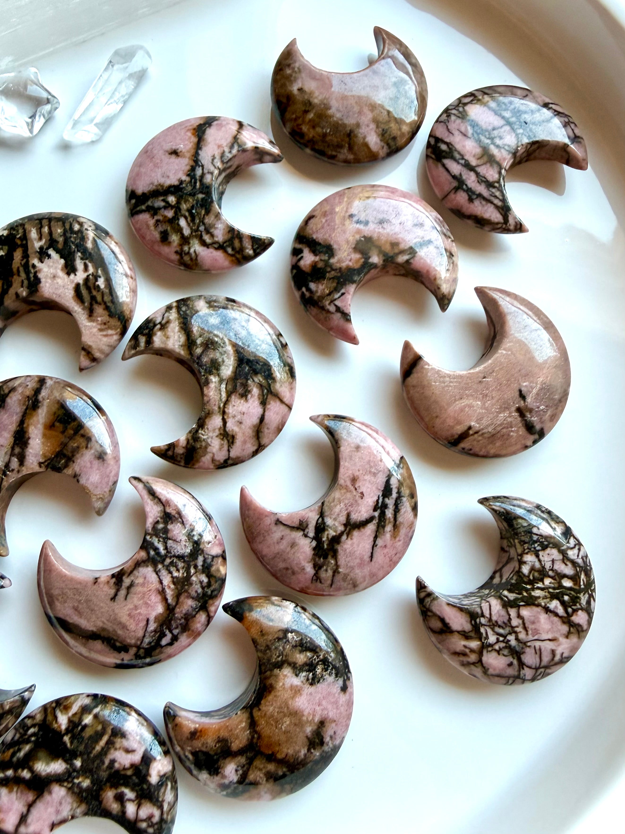 Rhodonite crescent moon crystals with unique natural veining and polished finish displayed on a white tray