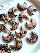 Rhodonite crescent moon crystals with unique natural veining and polished finish displayed on a white tray