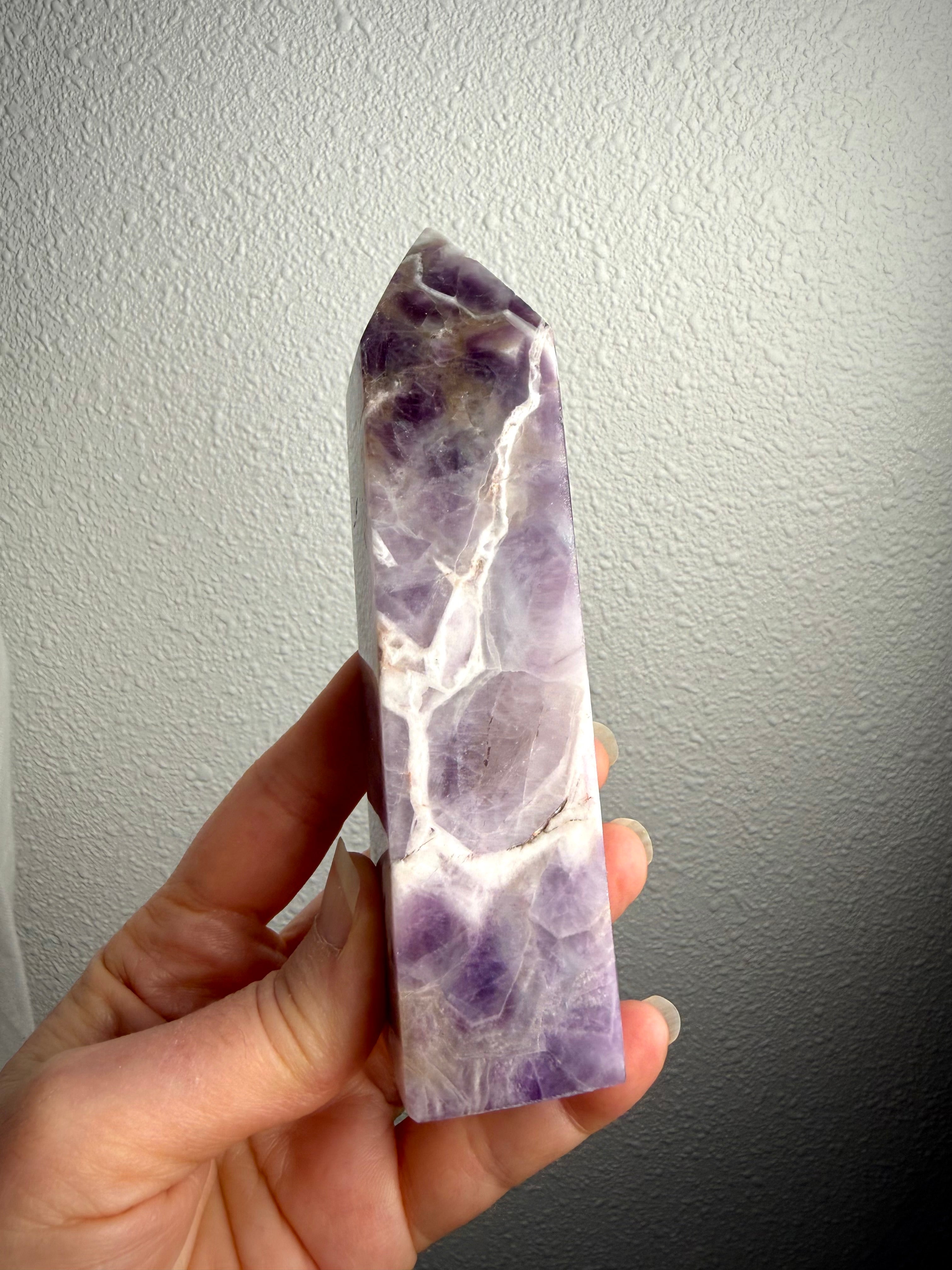 Dream Amethyst crystal point held in hand, showing its slender profile, lavender coloring and distinctive white quartz banding