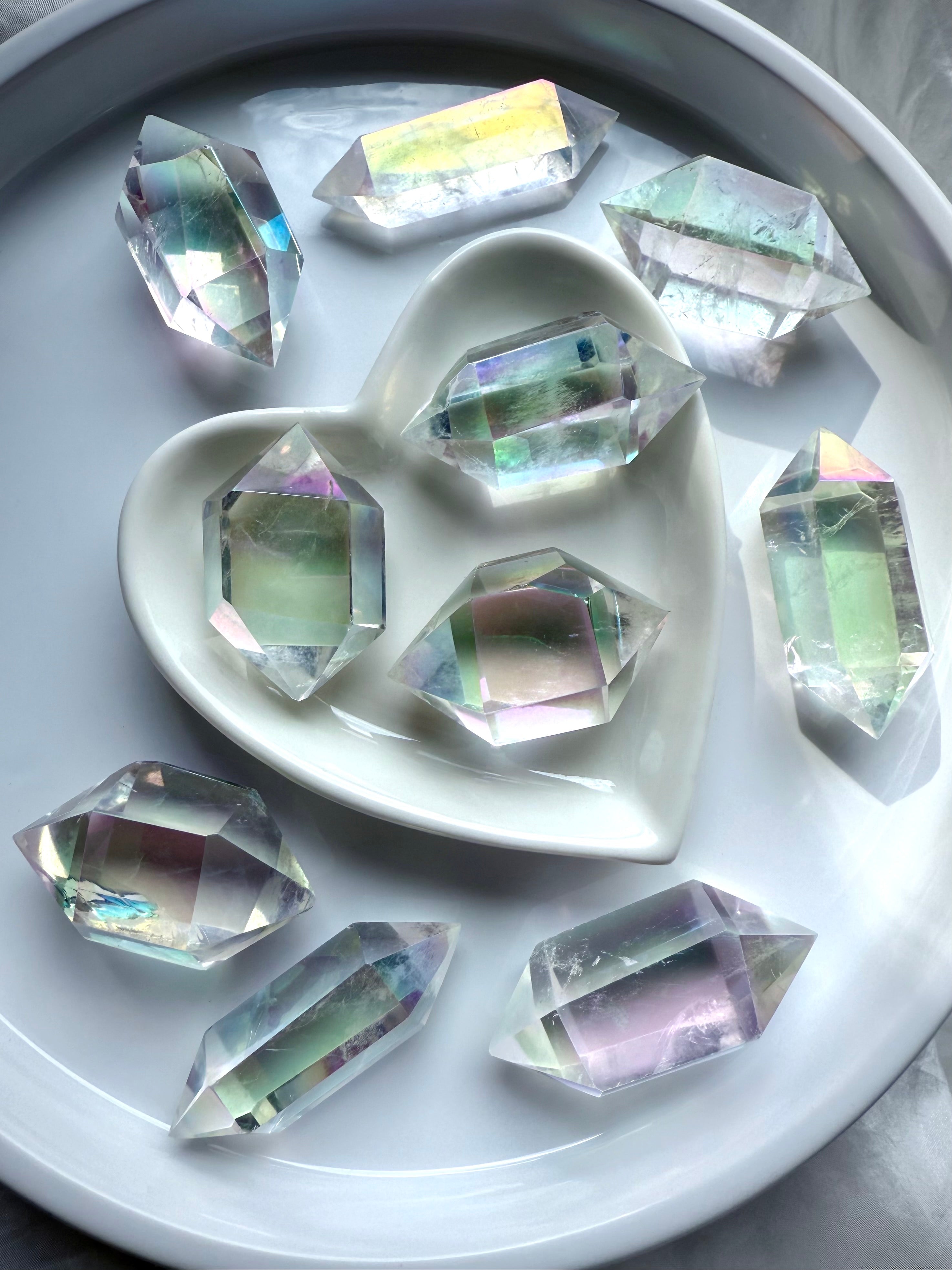Group of Angel Aura Quartz DT crystals with iridescent rainbow aura coating, arranged in a heart bowl and white dish