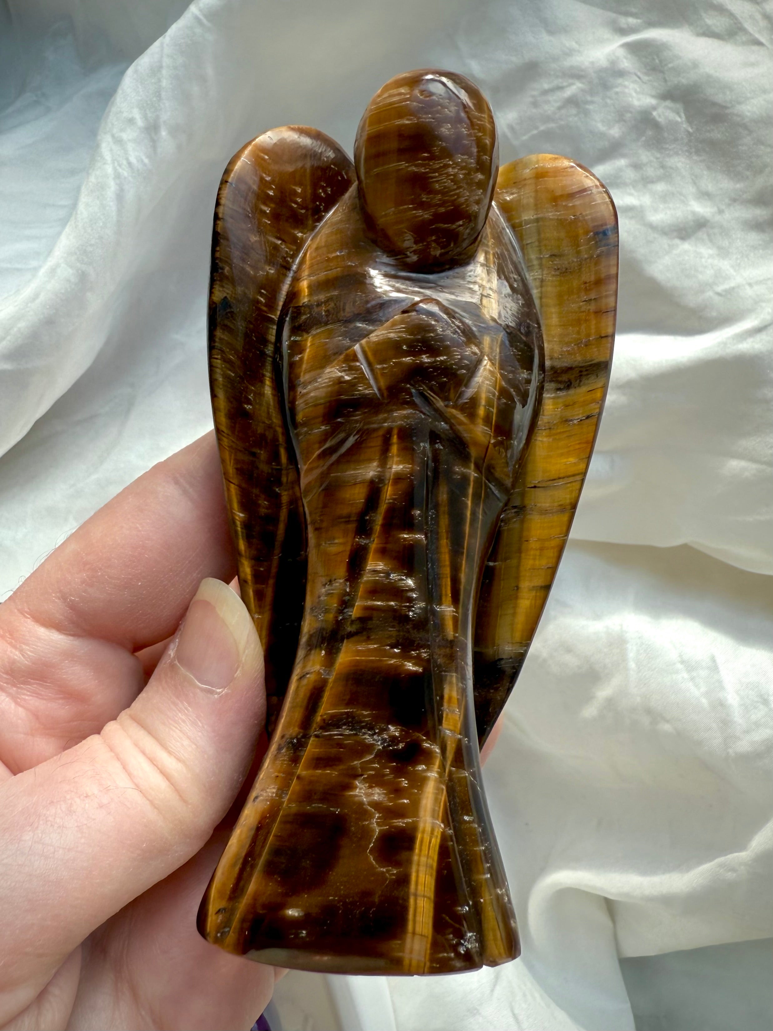 Hand holding Tiger’s Eye angel figurine with strong contrast in golden brown hues, emphasizing its guardian shape