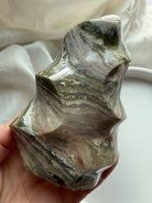 Hand-held view of Green Ocean Jasper flame highlighting its layered green, cream, and beige patterns in a glossy finish.