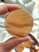 Closeup of a honey calcite meditation stone held between fingers, highlighting its soft golden hue and natural striations.