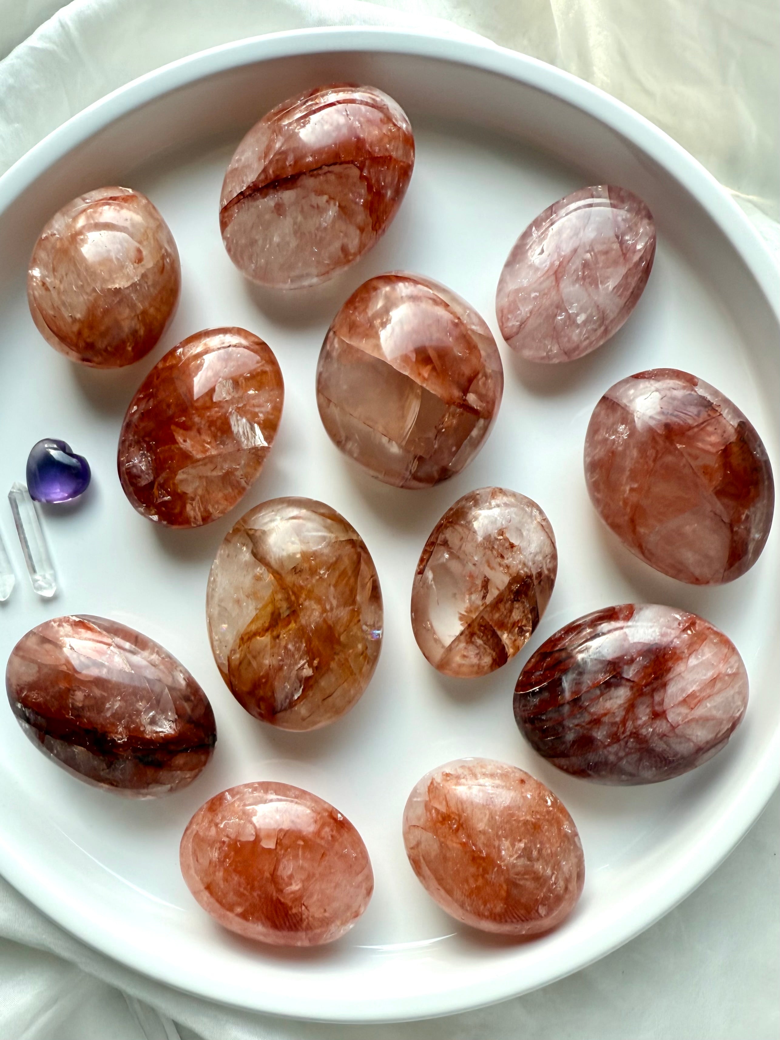 Assortment of polished Fire Quartz palm stones displayed in a white dish for energy healing rituals