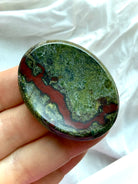 Polished Dragon Blood Stone worry stone showing a smooth thumb groove, mossy green coloring and natural red mineral inclusions