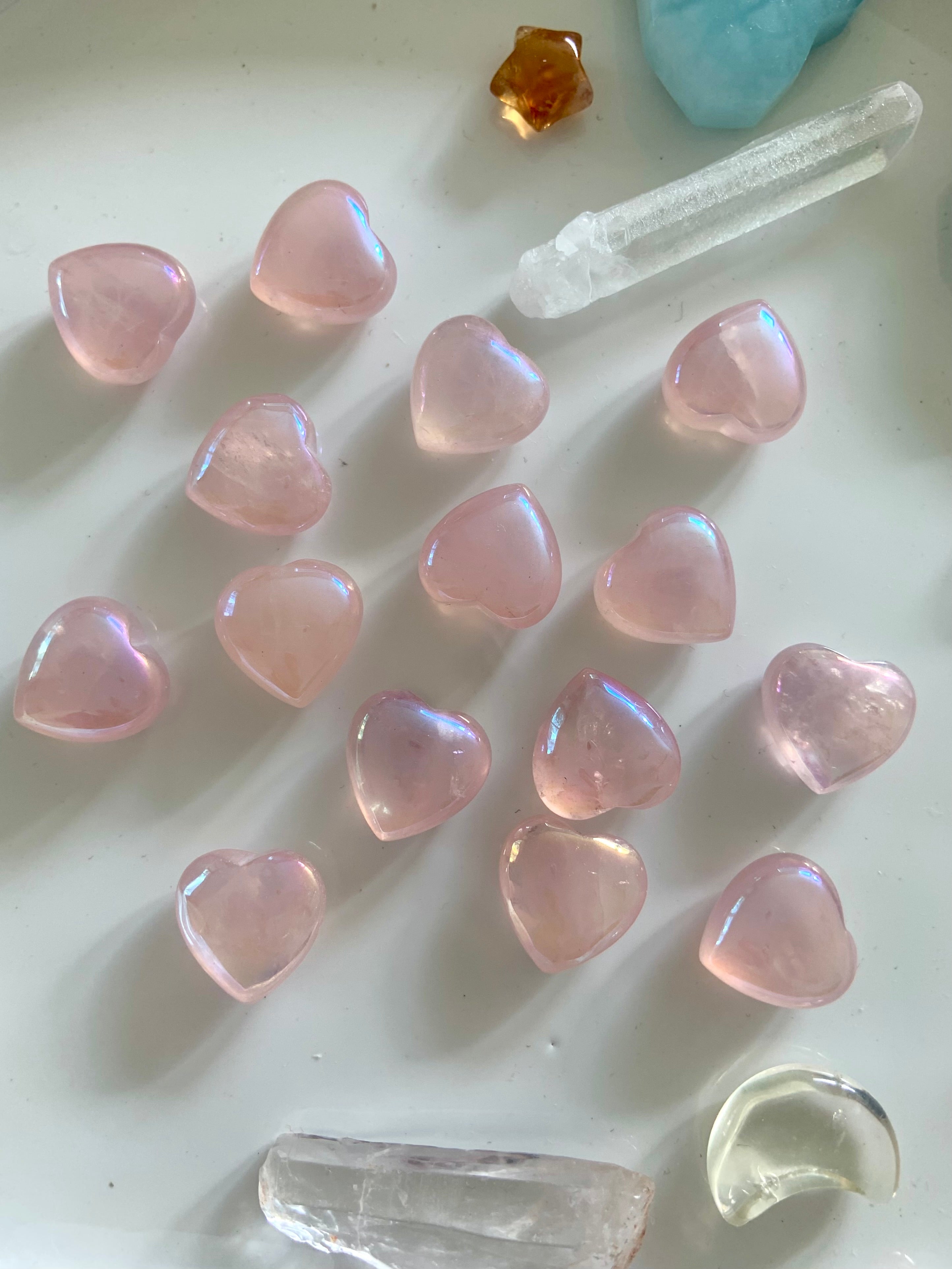 Flatlay of iridescent aura rose quartz hearts with other crystals on a white background — radiant heart chakra stones for spiritual love & peace