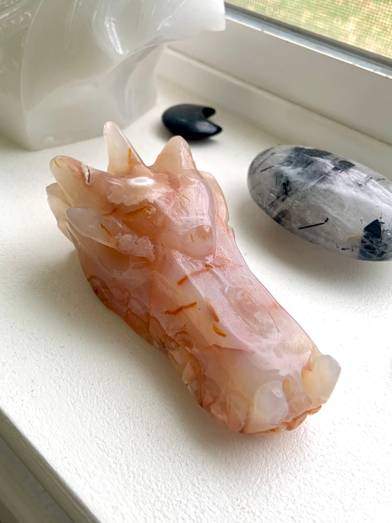 Carnelian Flower Agate Dragon Head Carving photographed in natura light on a windowsill with some other crystals