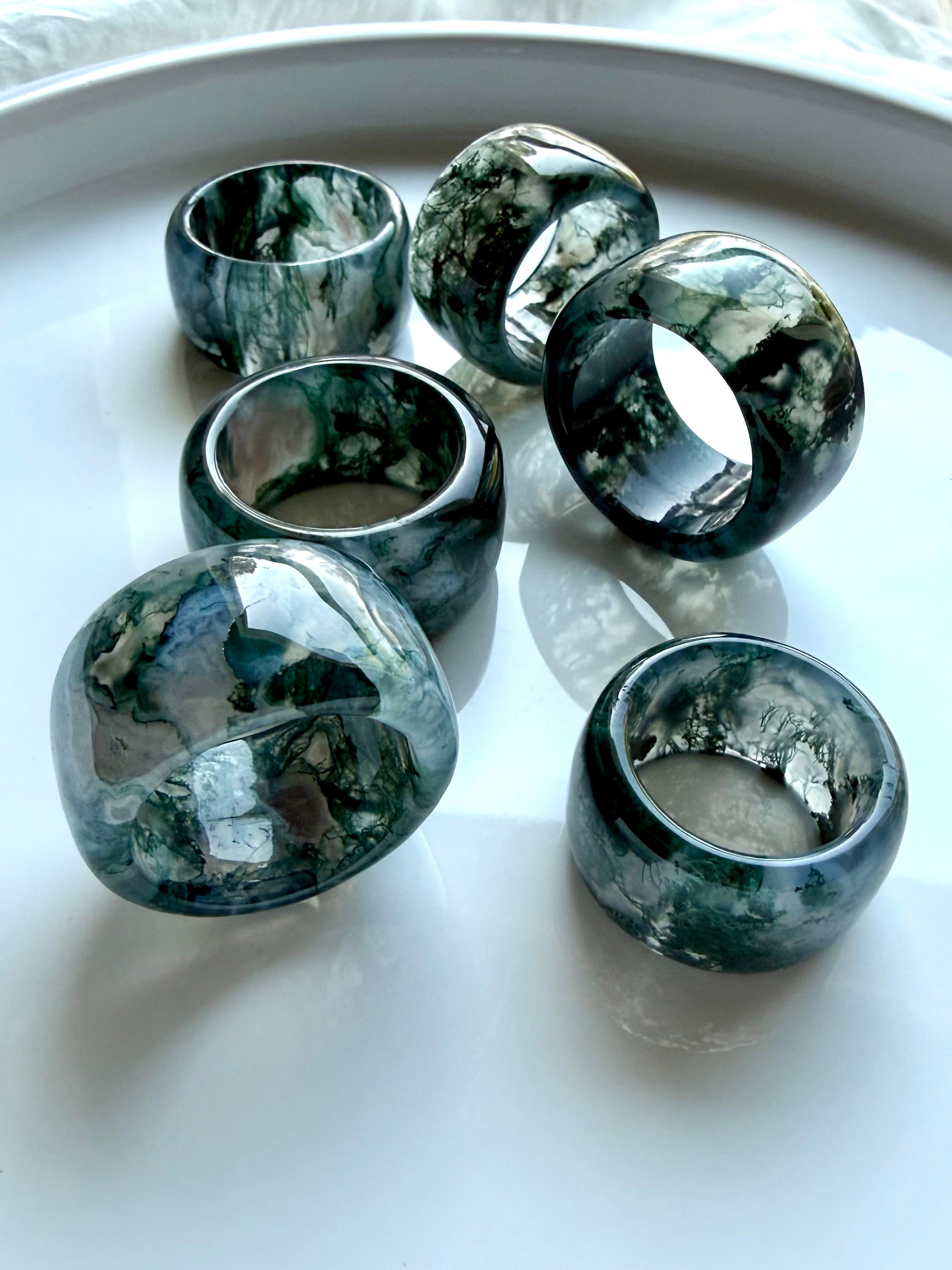 polished moss agate wide band rings grouped together on marble surface with translucent depth and organic natural patterns