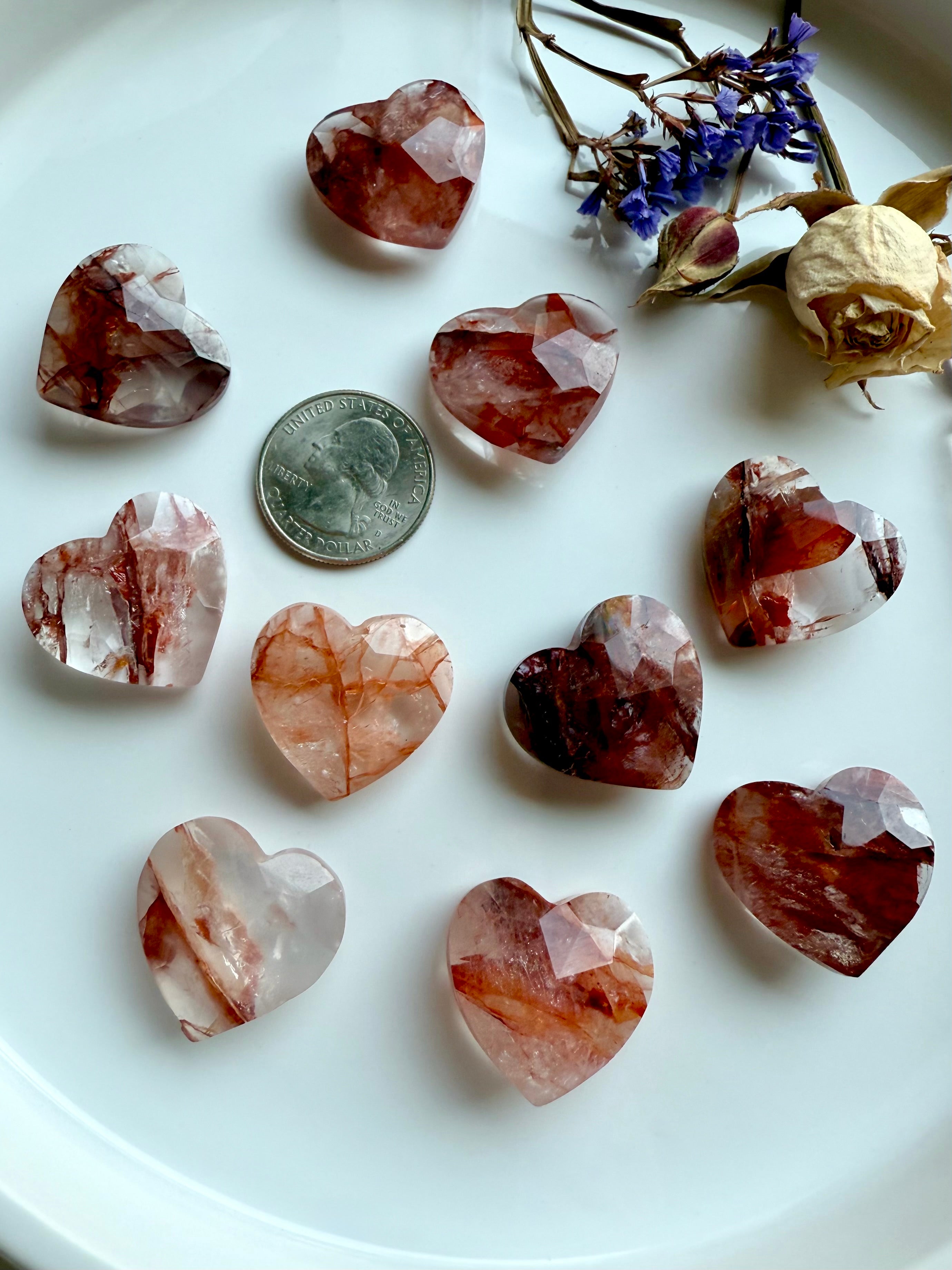 Faceted Fire Quartz hearts in white bowl with quarter for size reference – hand-carved grounding crystals for Root Chakra energy healing