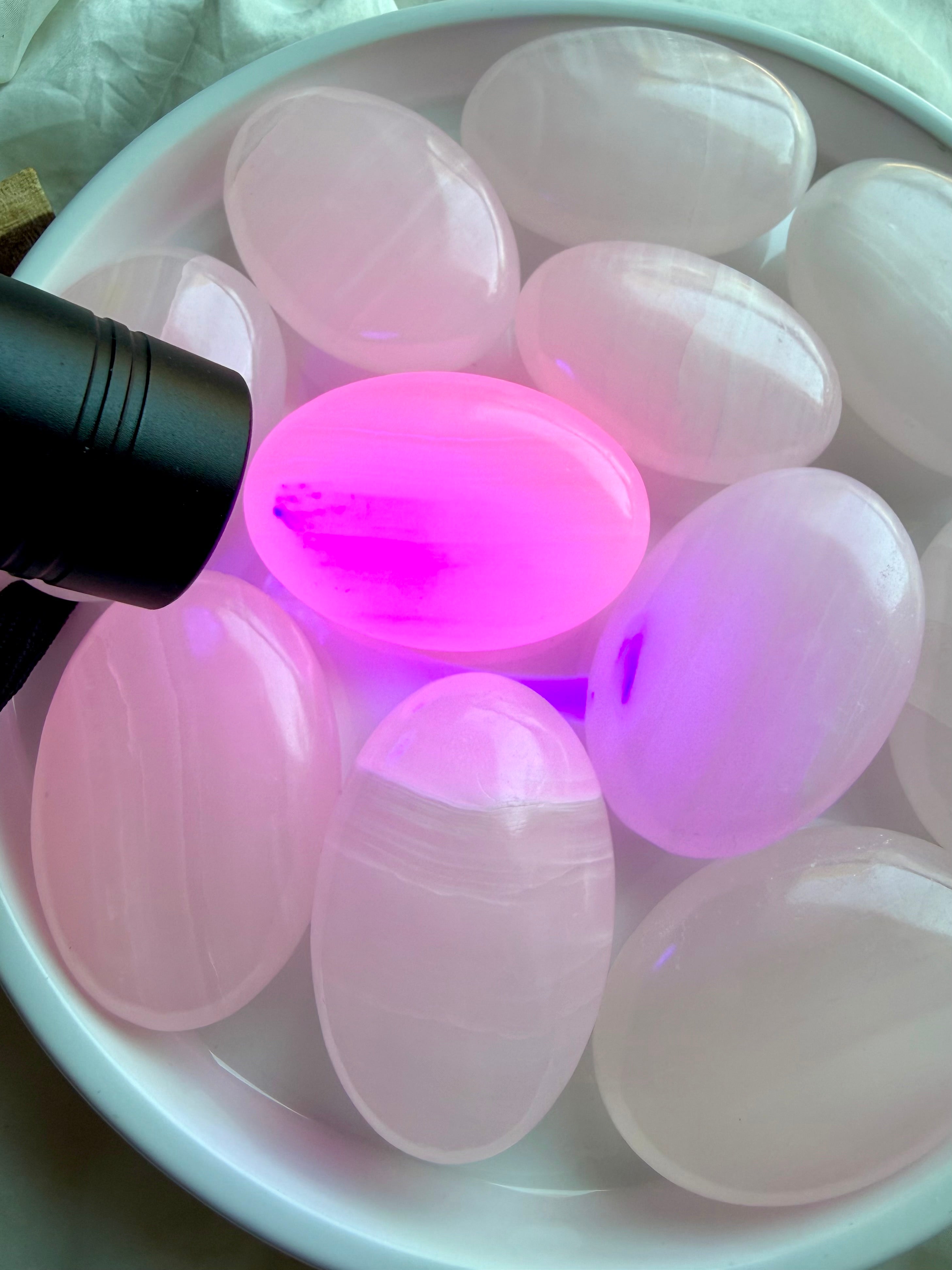 Mangano Calcite palm stones glowing bright pink under UV light showing natural fluorescence