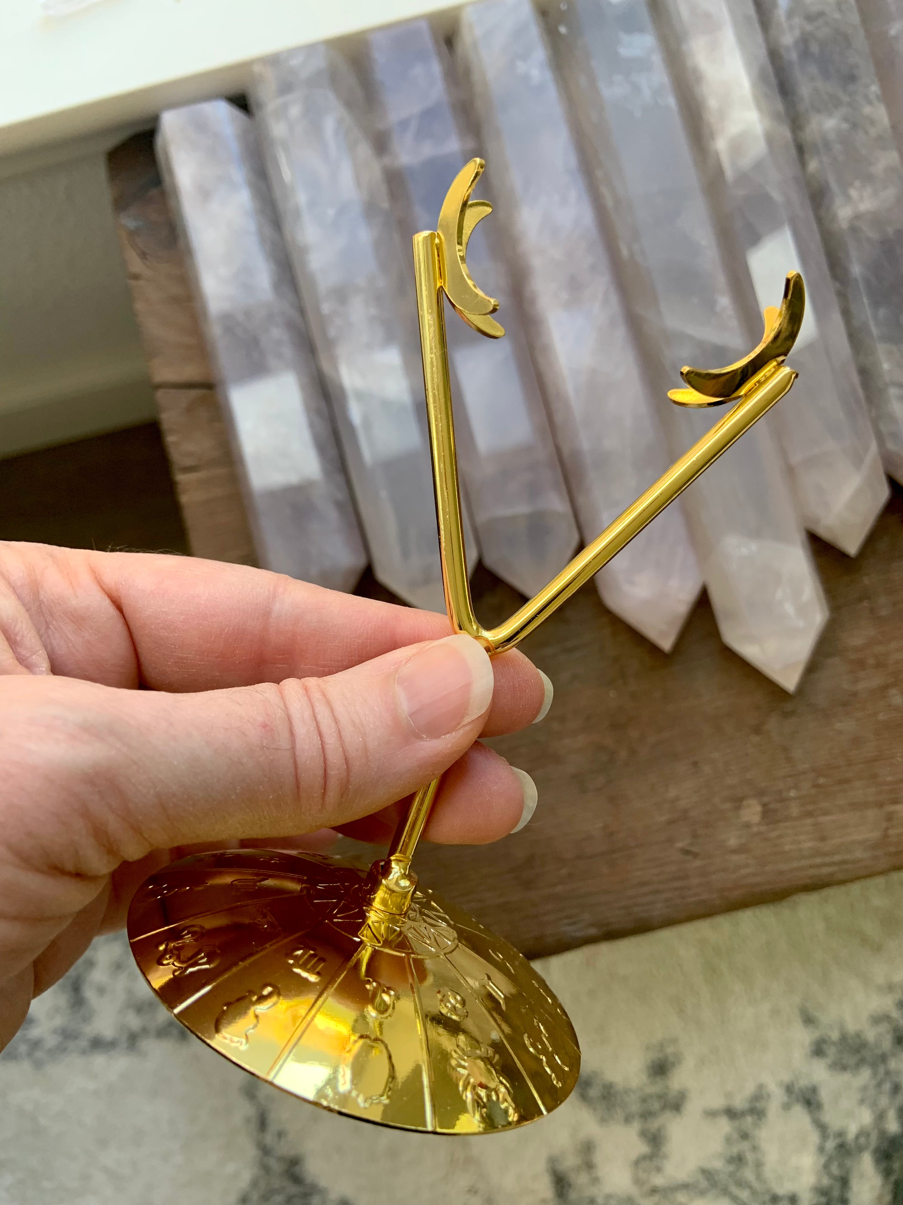 Gold crystal display stand held in hand to show scale — features zodiac wheel base & moon-shaped prongs
