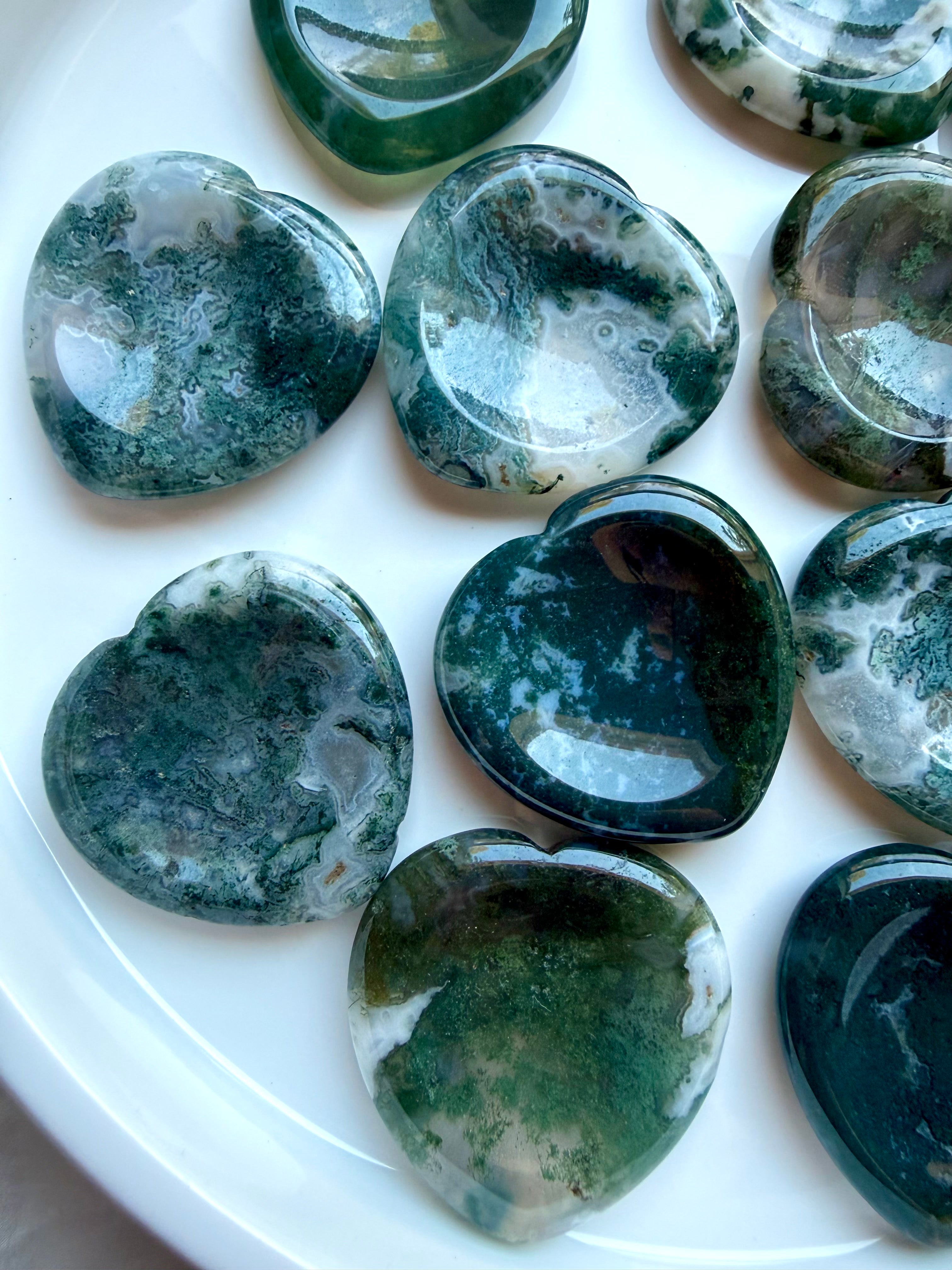 Assorted Moss Agate heart worry stones displayed on a white plate with natural moss patterns and polished finish