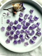 Mini amethyst moon and star carvings in soft violet hues arranged on a white ceramic tray with crystals and dried flowers