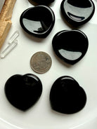 Black obsidian heart worry stones shown with quarter for size scale