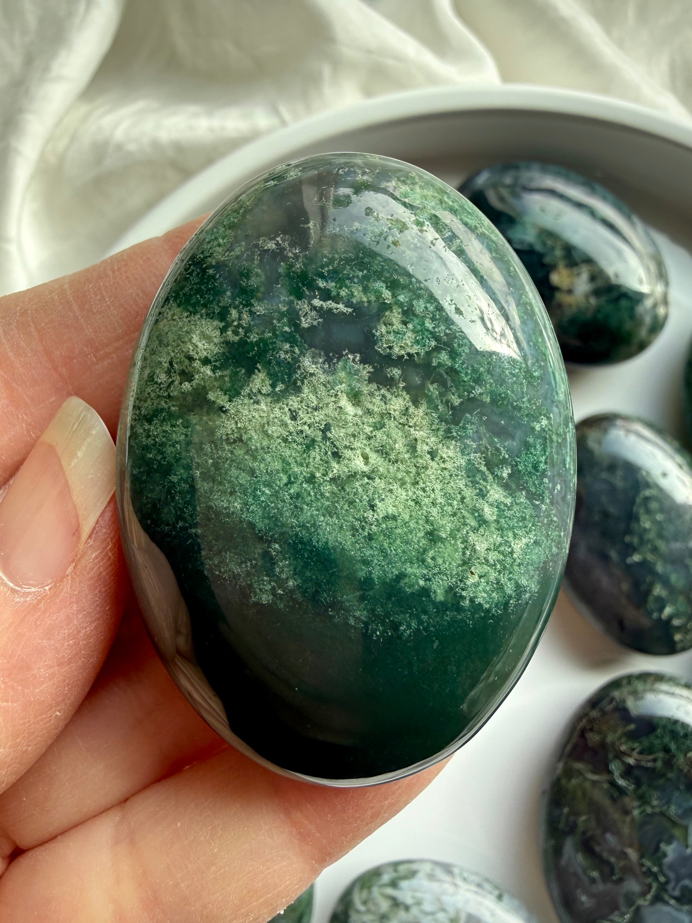 Close-up of moss agate palm stone in hand with translucent green inclusions, grounding stone for meditation and stress relief
