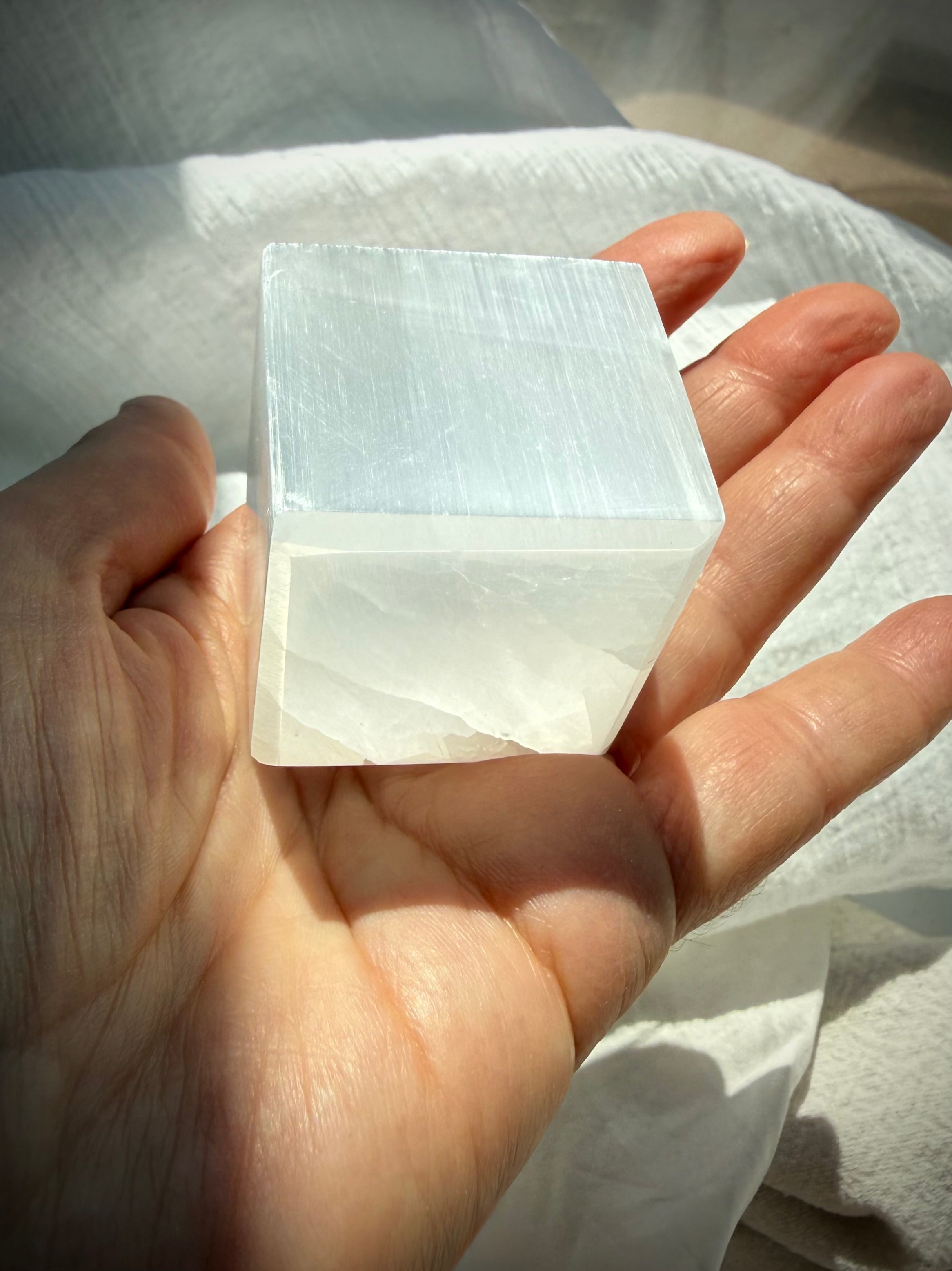 Selenite cube held in palm showing luminous white layers and smooth polished crystal faces