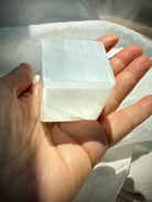 Selenite cube held in palm showing luminous white layers and smooth polished crystal faces