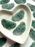 Close up of Blue Water Jade butterfly crystal carvings displayed in ceramic heart bowl