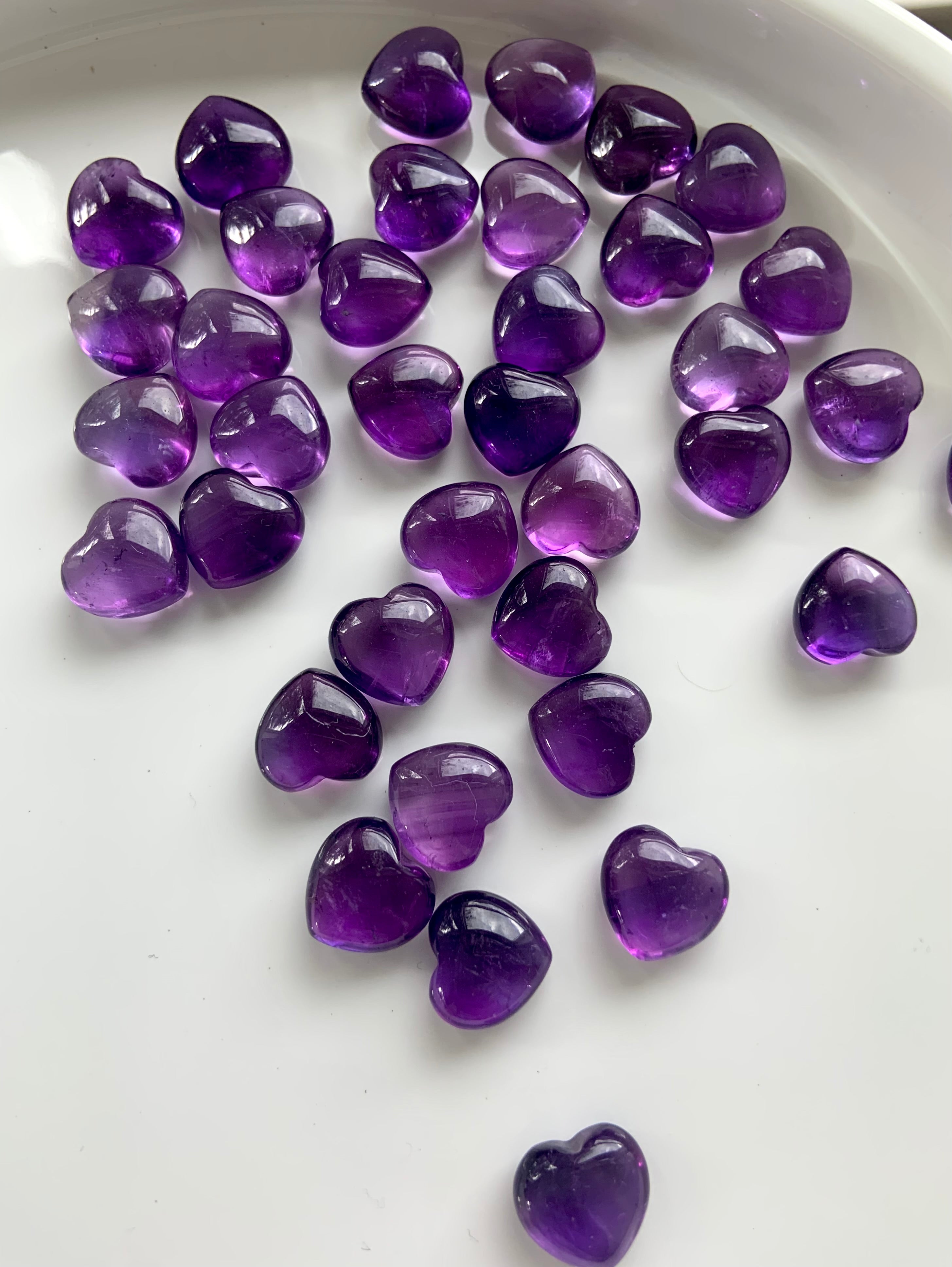Wide angle view of scattered mini sized Amethyst hearts on a white plate — radiant crystals for divine guidance