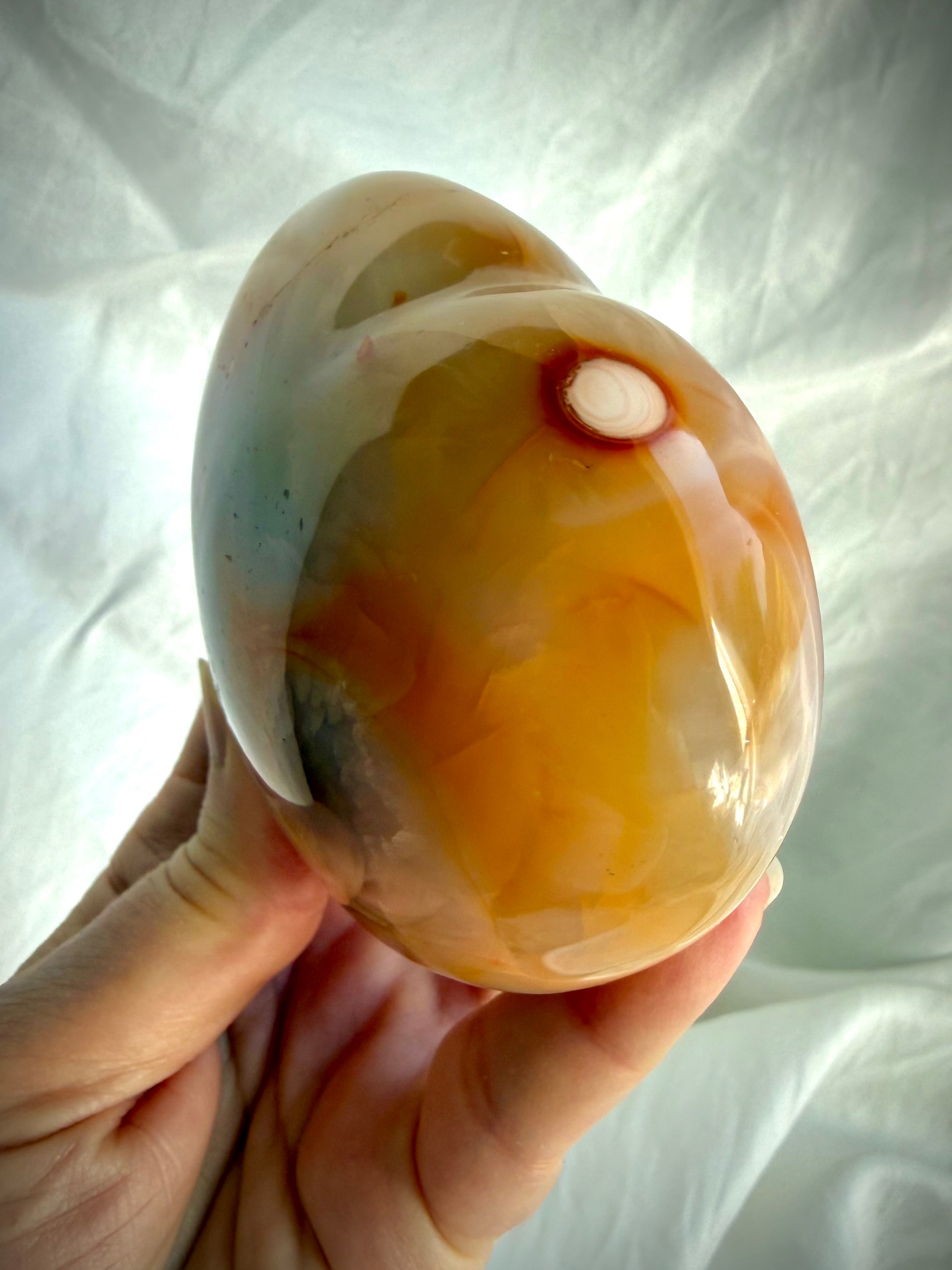Side view of polished Carnelian heart crystal highlighting thickness, curved profile and natural orbicular pattern