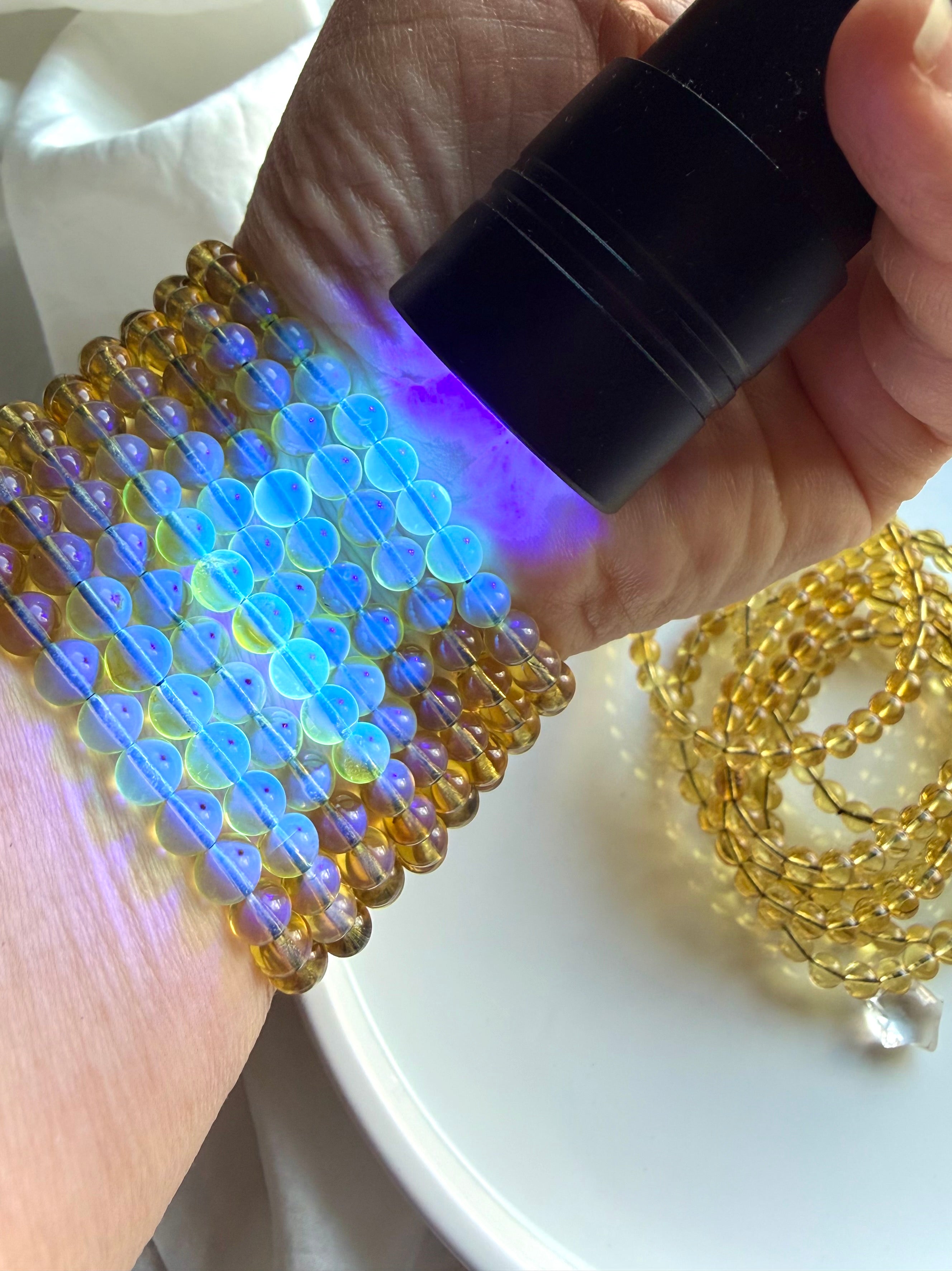 Blue amber crystal bead bracelet glowing under UV flashlight – Indonesian UV reactive amber