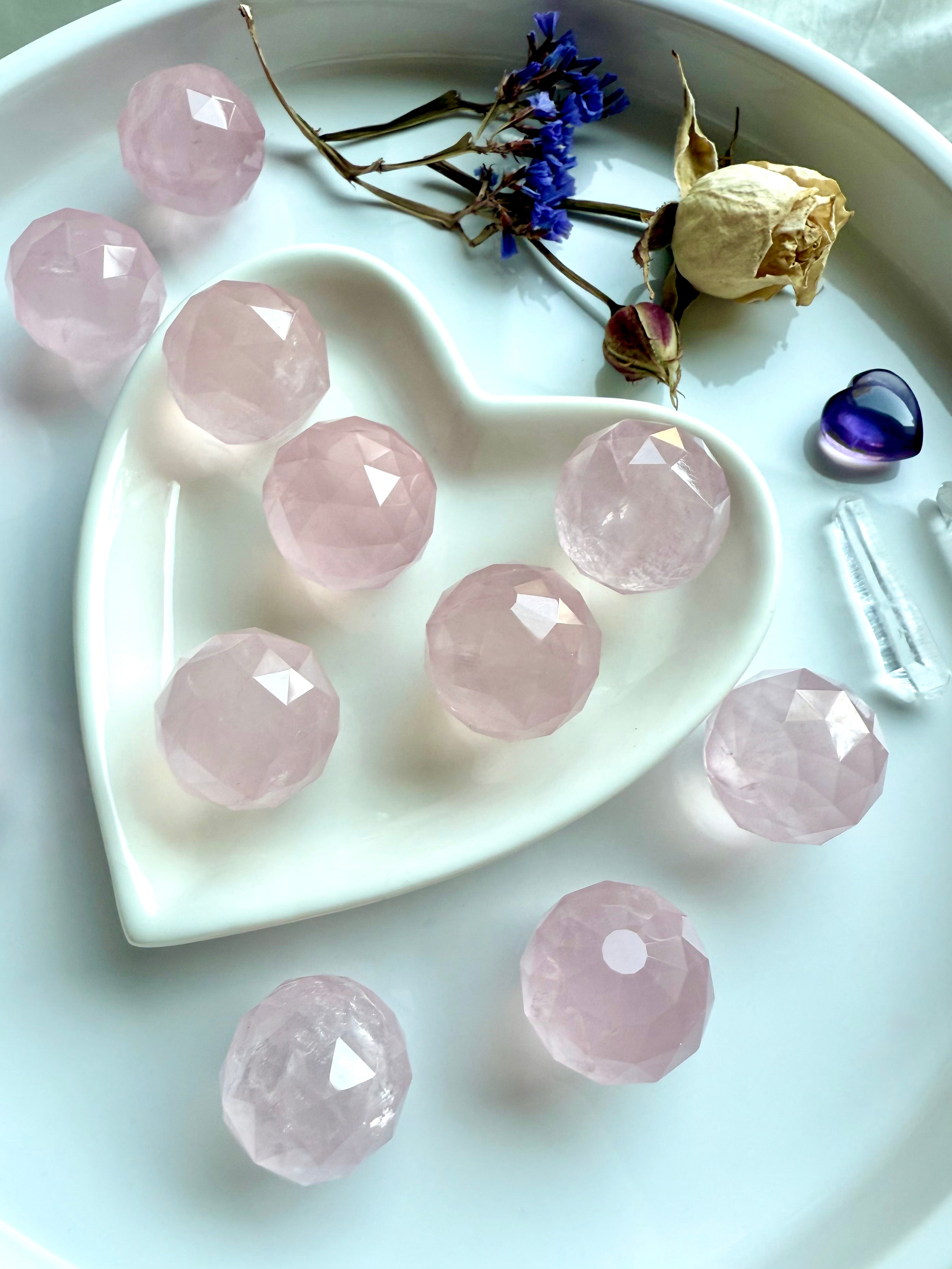 Mini faceted rose quartz crystal spheres on a heart-shaped white dish with dried flowers and crystals. Dreamy pink stones for heart chakra healing.